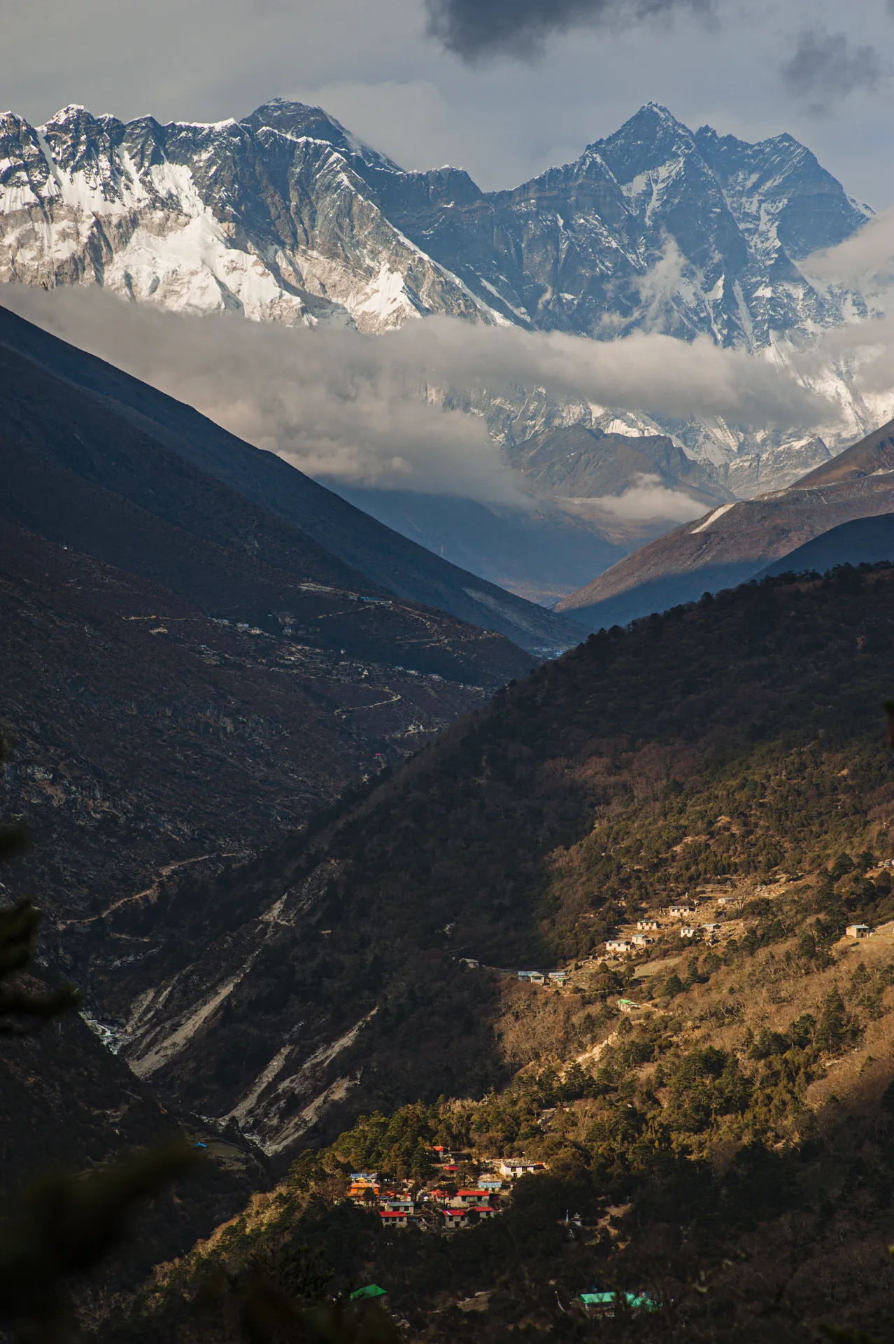 View toward the Everest, Lhotse and Nuptse massif from a Khumbu ridge with a forested village clinging to the slope below.