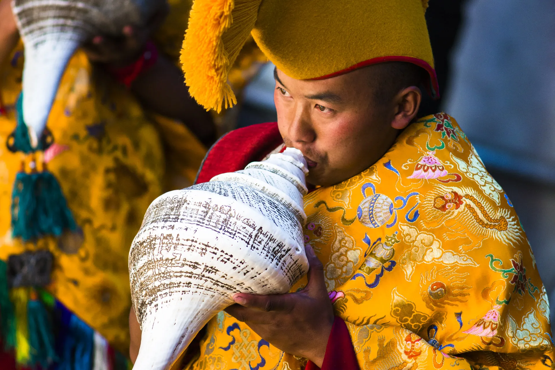 A Tibetan Buddhist monk in a yellow ceremonial hat blows a long carved conch shell during a ceremony in the Khumbu valley.