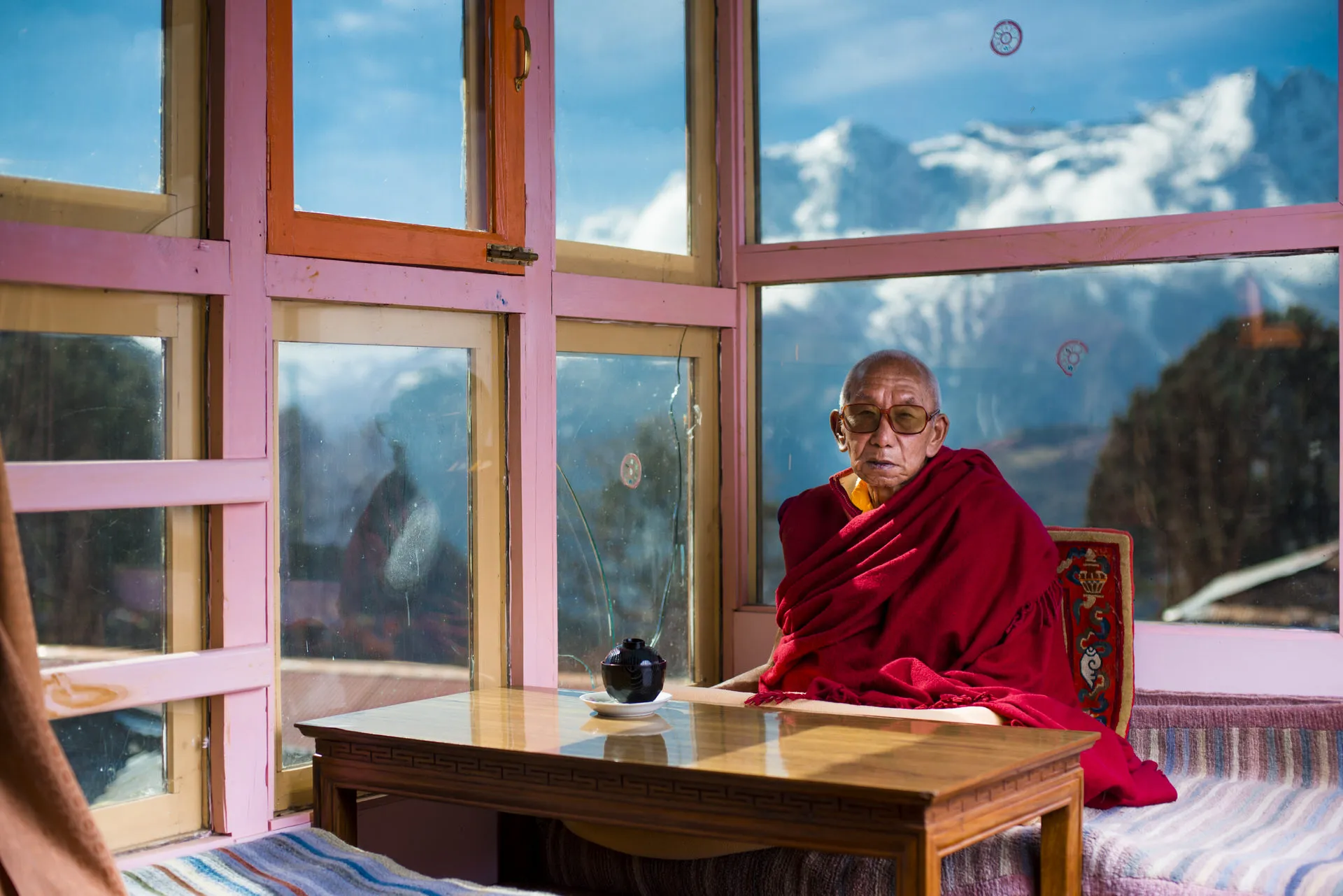 The head lama of Tengboche monastery sits in a pink window-walled receiving room with a view onto snow-capped Himalayan peaks beyond.