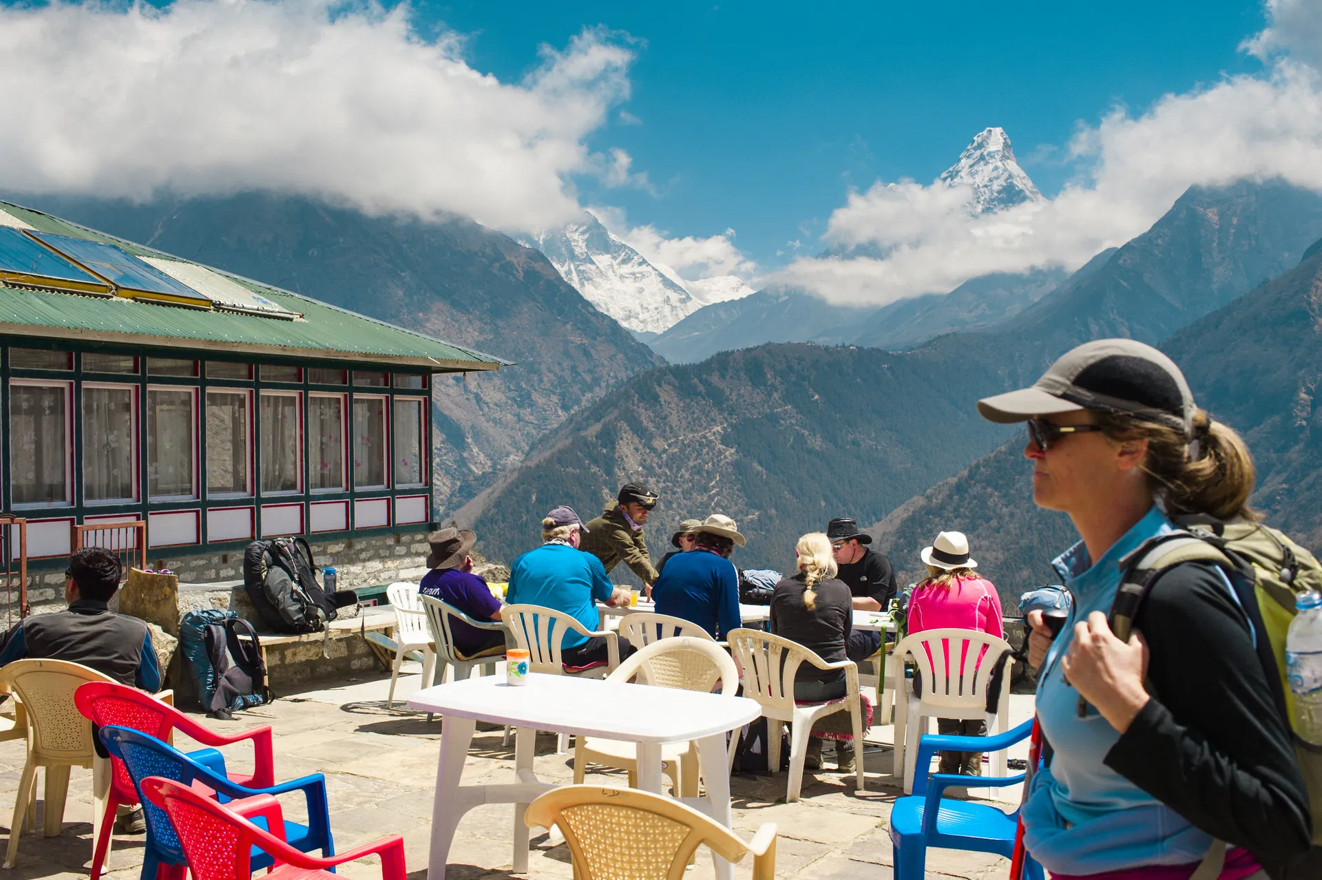 Trekkers eat lunch on the patio of a Khumbu teahouse with the sharp peak of Ama Dablam visible across the valley.