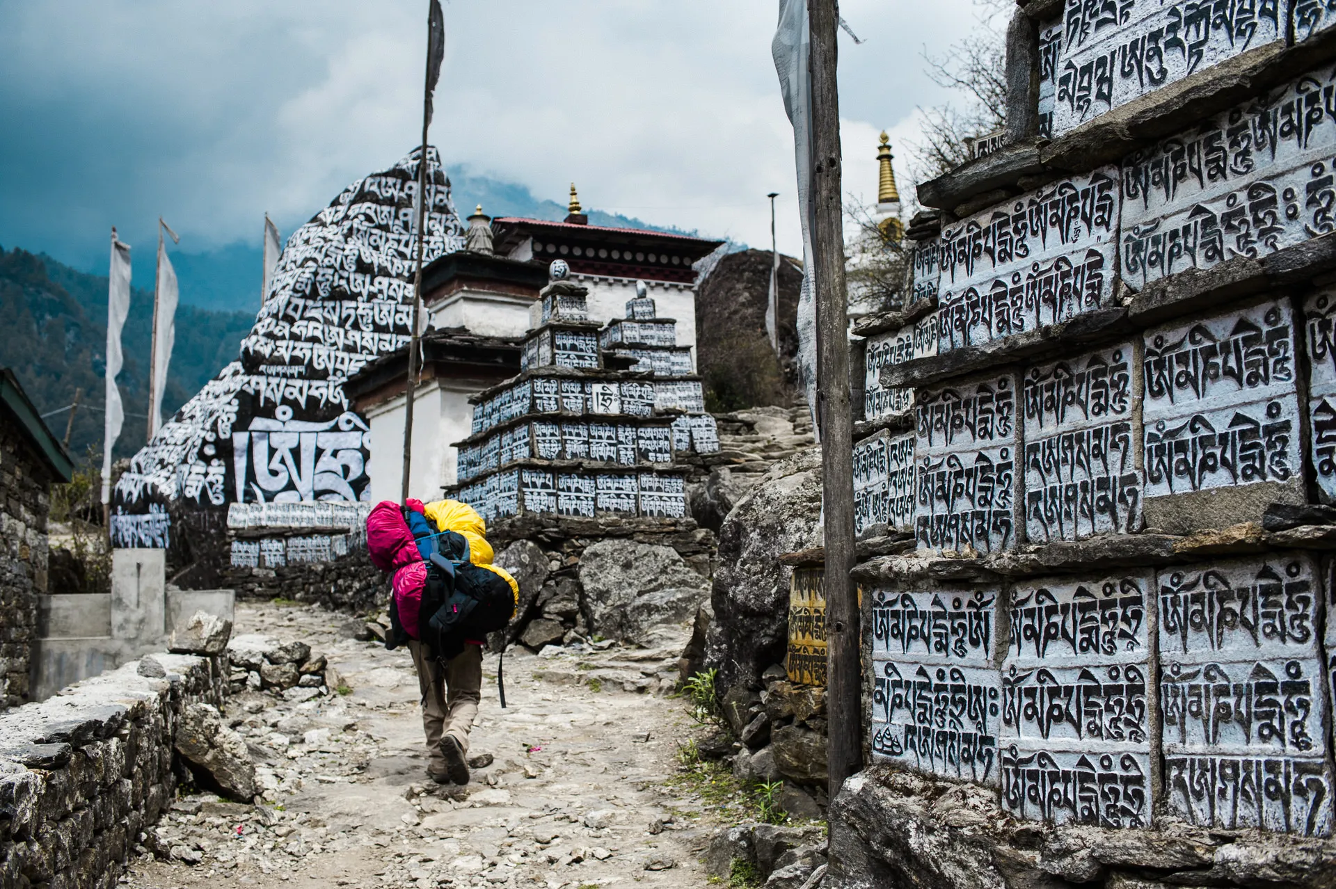 A porter carrying a heavy load walks past a long mani-stone wall carved with Buddhist mantras on the trail to Mt Everest.