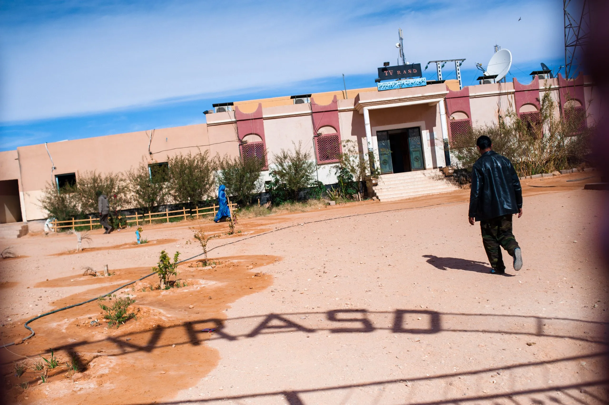 A man walks across a dirt yard toward the entrance of the TV RASD station building in Tindouf, Algeria.