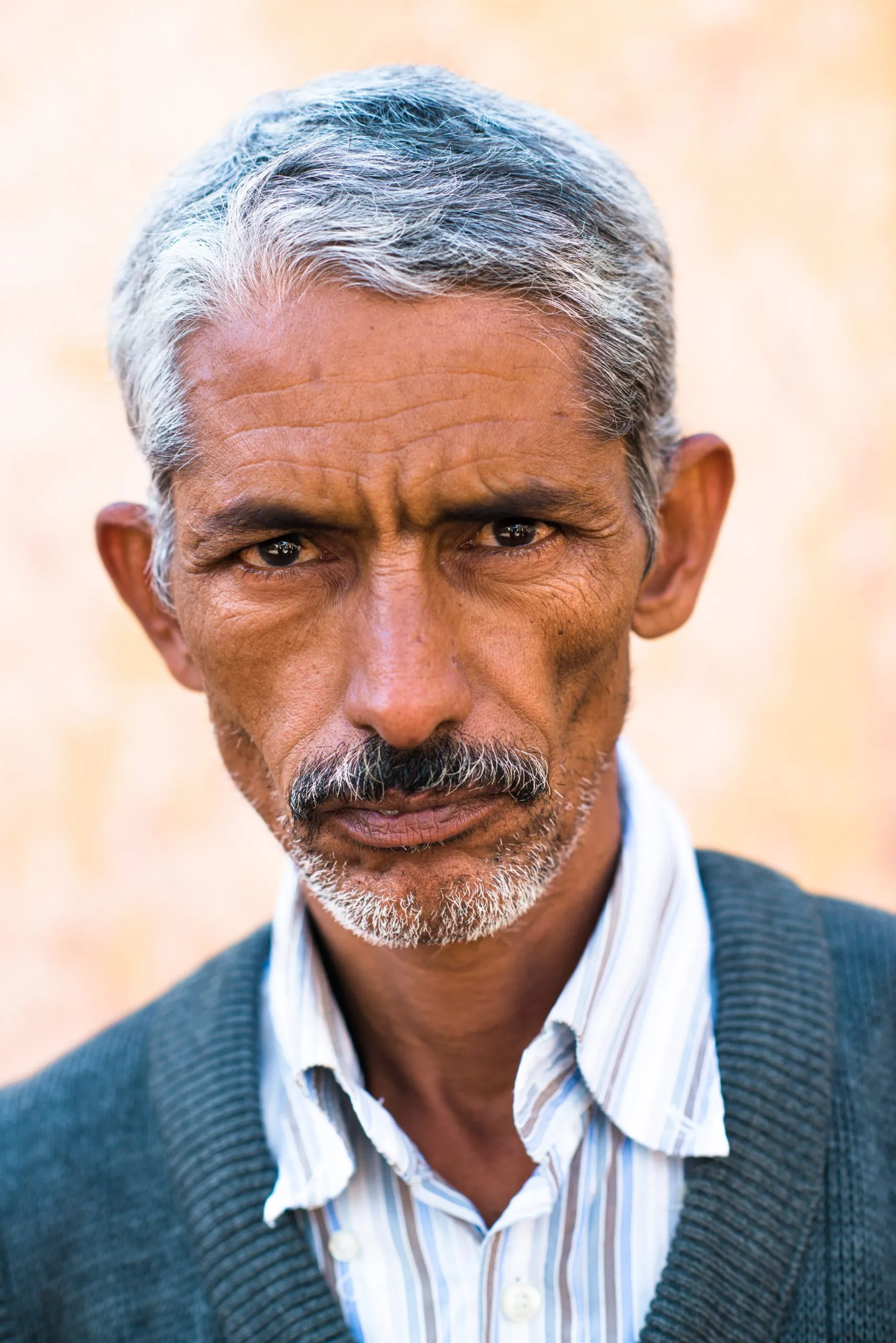 A close portrait of an older man with greying hair and a moustache, in a striped shirt and cardigan, in Tindouf.