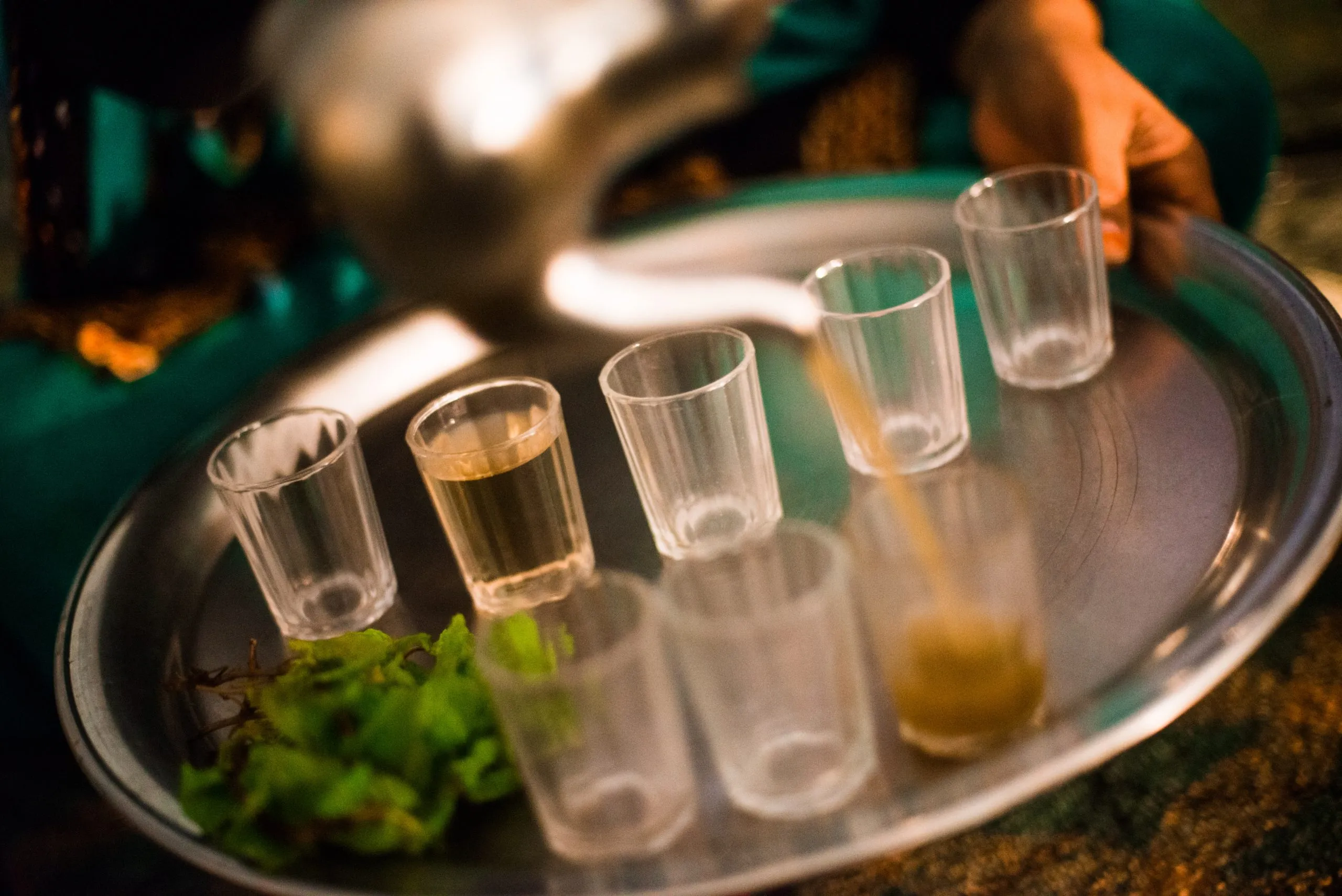 A close view of small glasses of mint tea poured on a silver tray, served in a tent in the Tindouf camp.