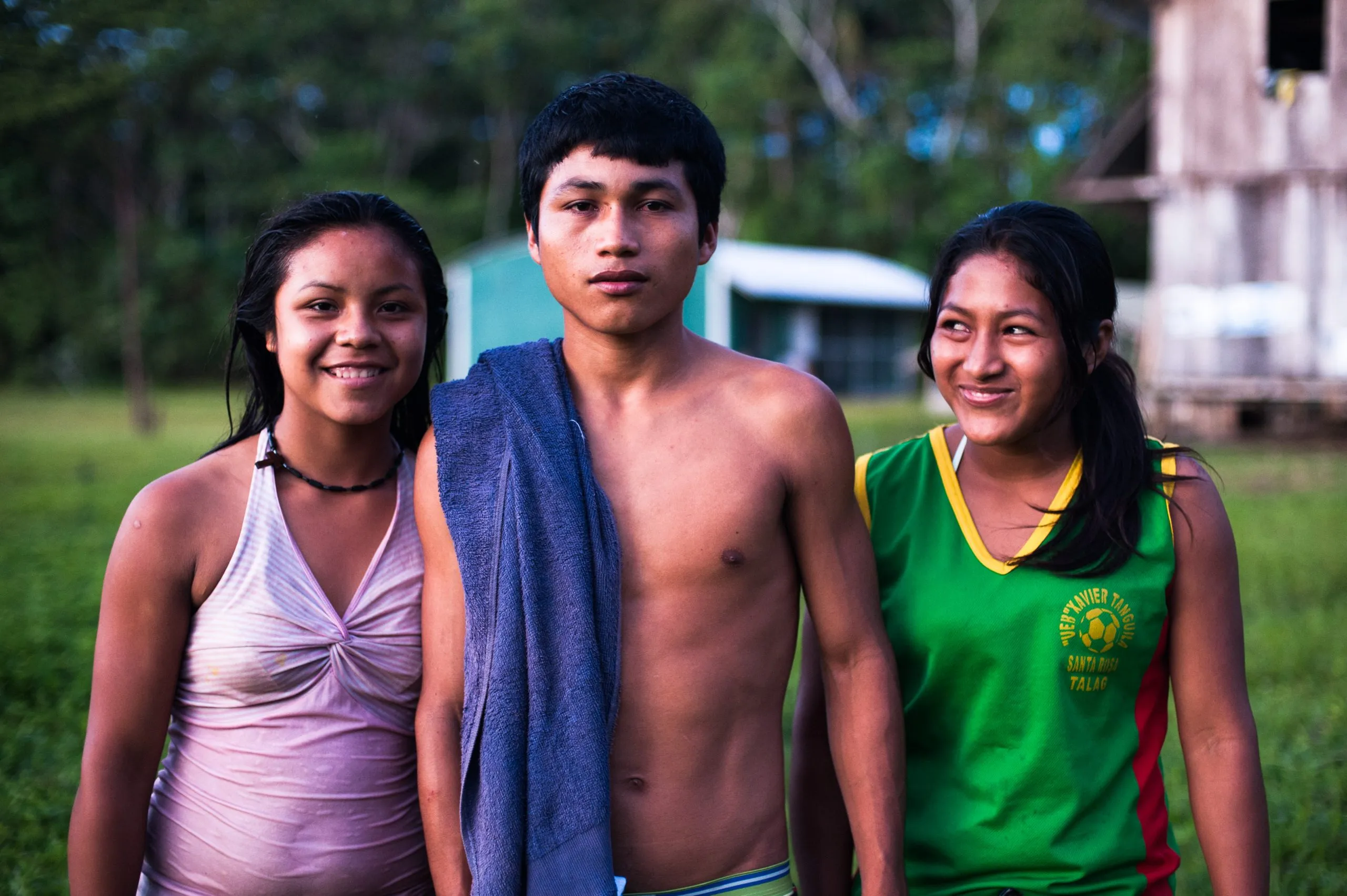 Three young Kichwa villagers stand together in soft afternoon light at the edge of an Ecuadorian Amazon community.