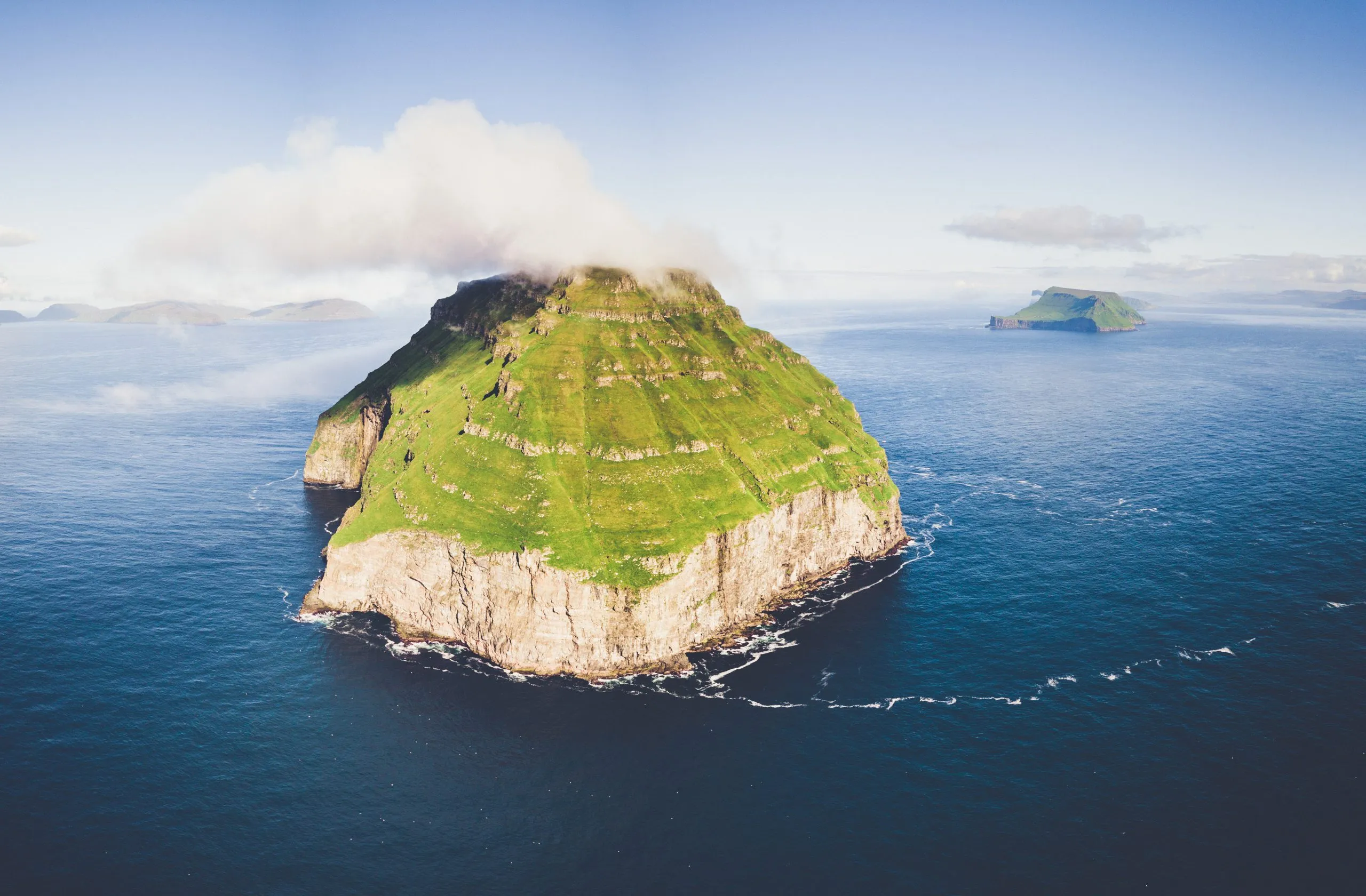 Drone panorama of Lítla Dímun, the small uninhabited green island of the Faroe Islands rising from the North Atlantic under a cap of cloud.
