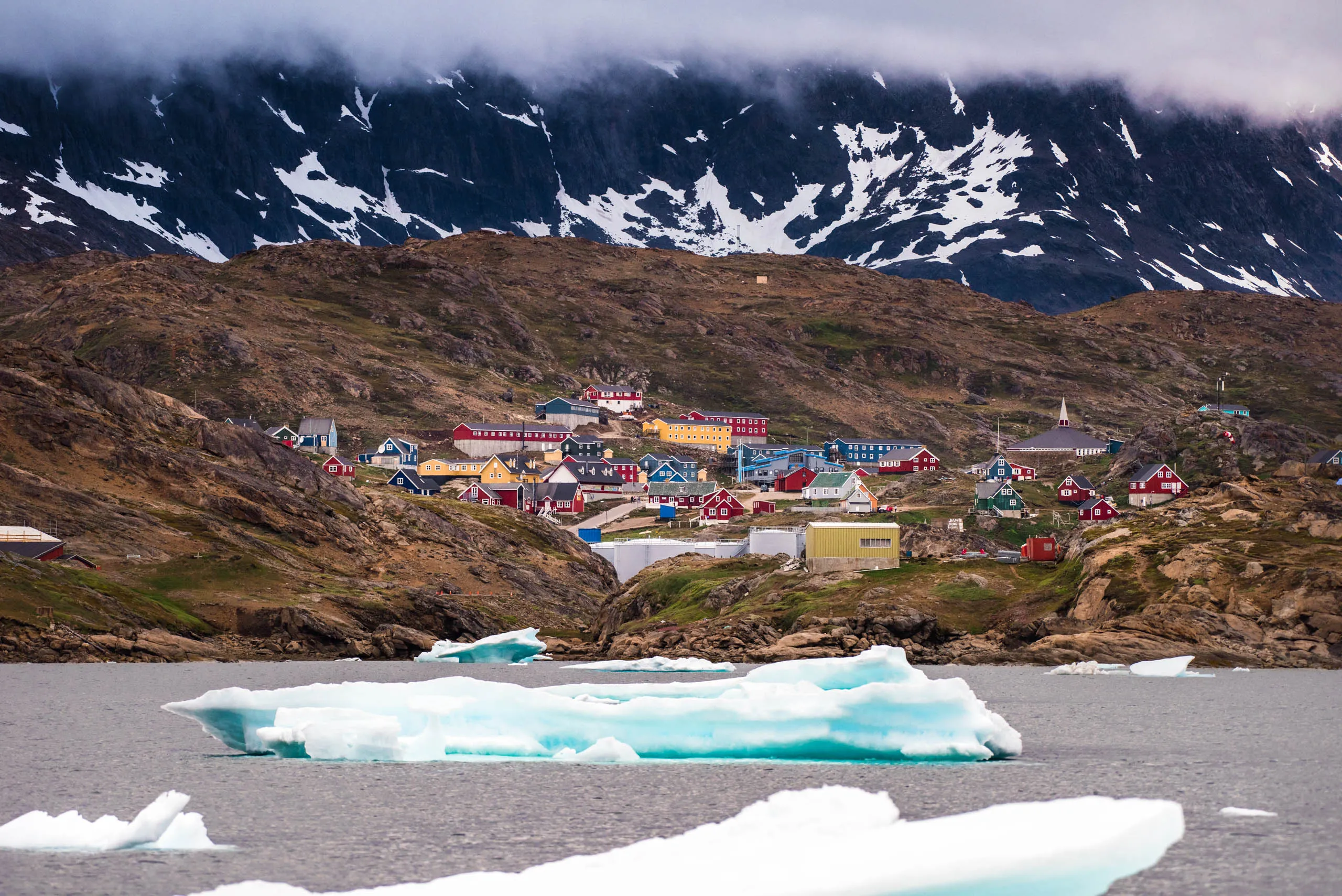 Colourful remote Arctic settlement seen from the water with icebergs floating in the foreground