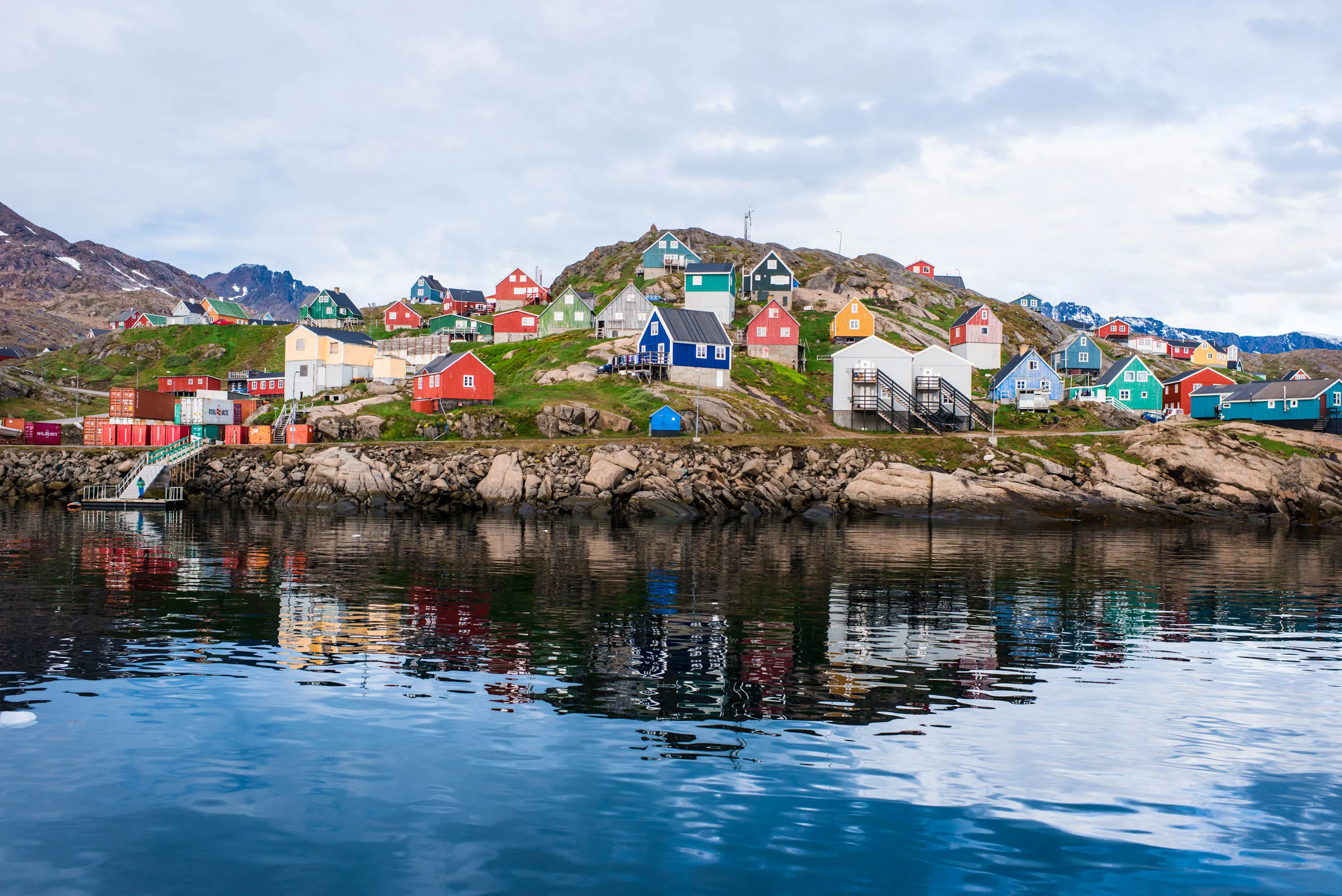 Colourful houses of a small Greenlandic coastal settlement reflected in calm harbour water