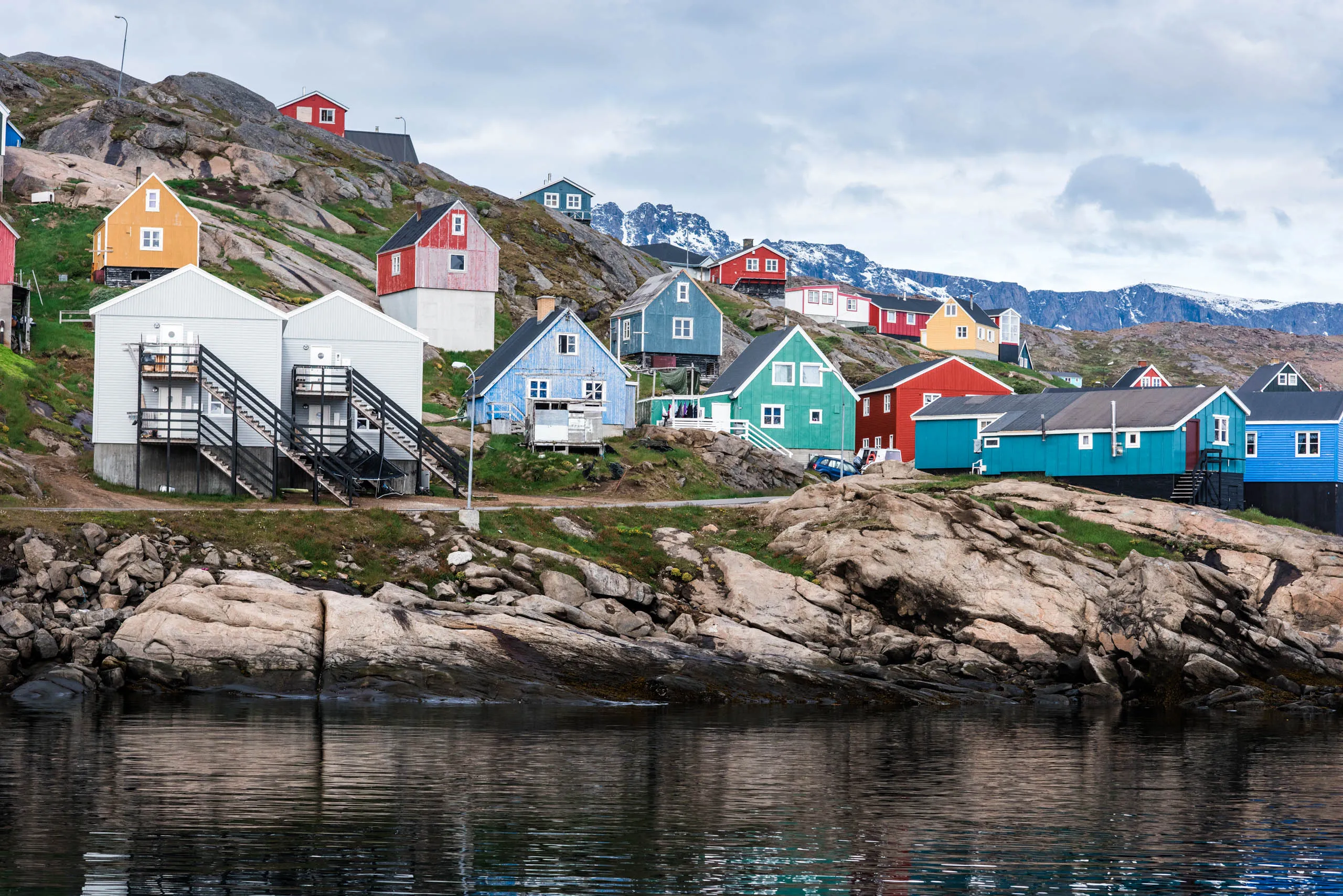 Colourful wooden houses clustered on a rocky Greenlandic shoreline under an overcast sky