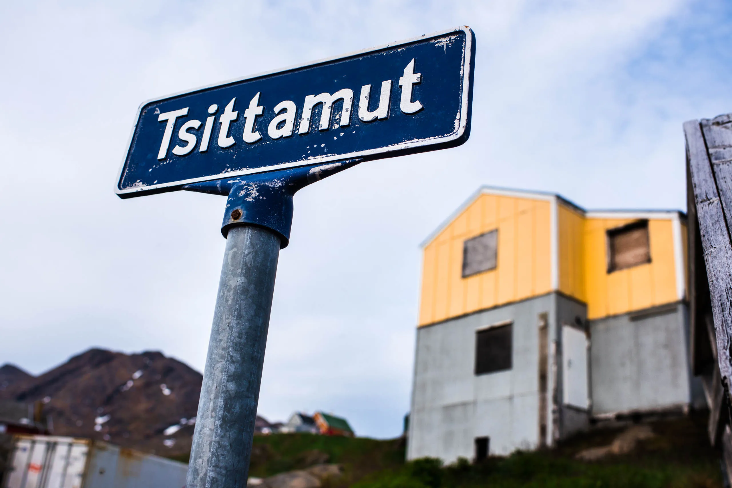 Weathered Tsittamut street sign in front of a yellow building in a Greenlandic village