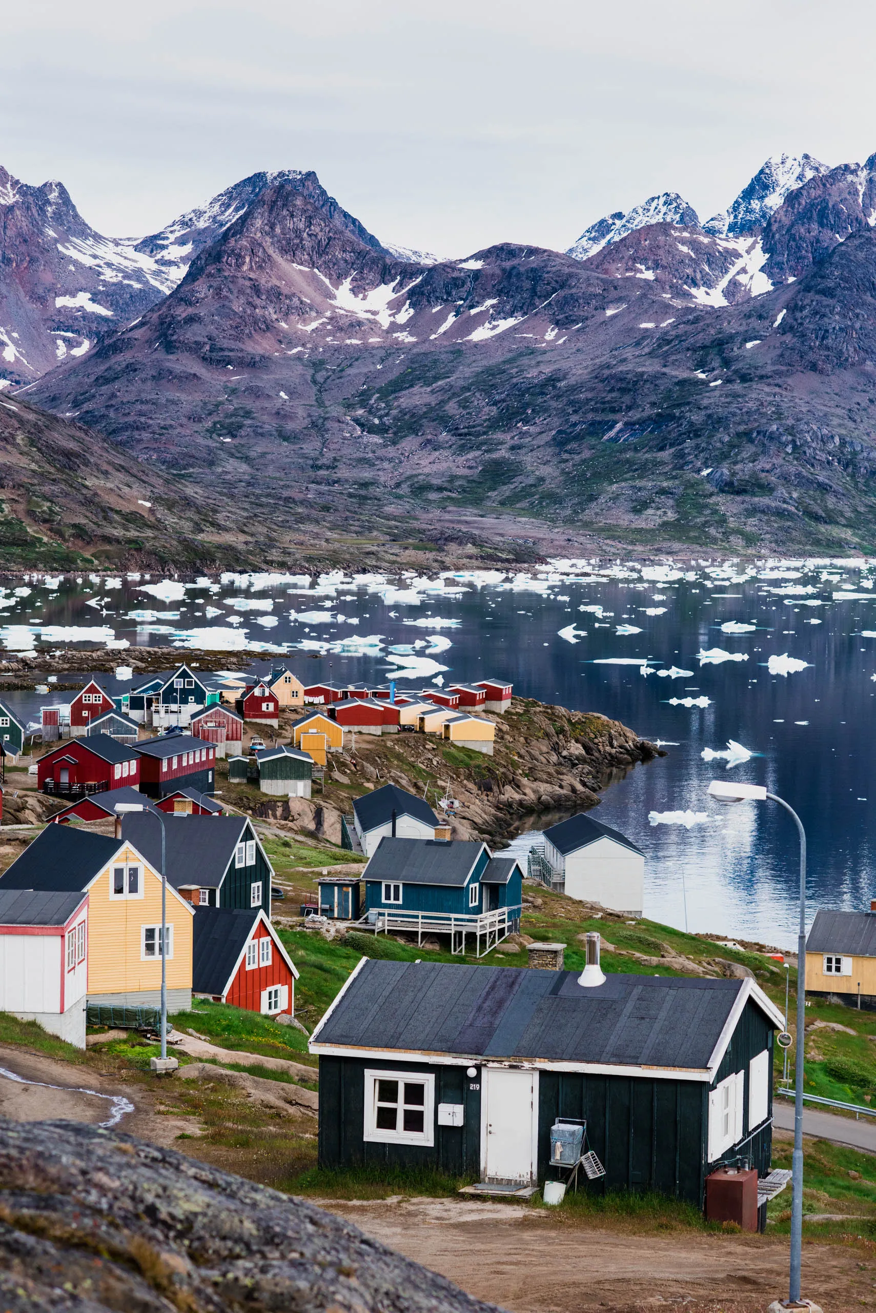 Colourful Greenlandic village houses spilling down a rocky hillside above an ice-dotted bay
