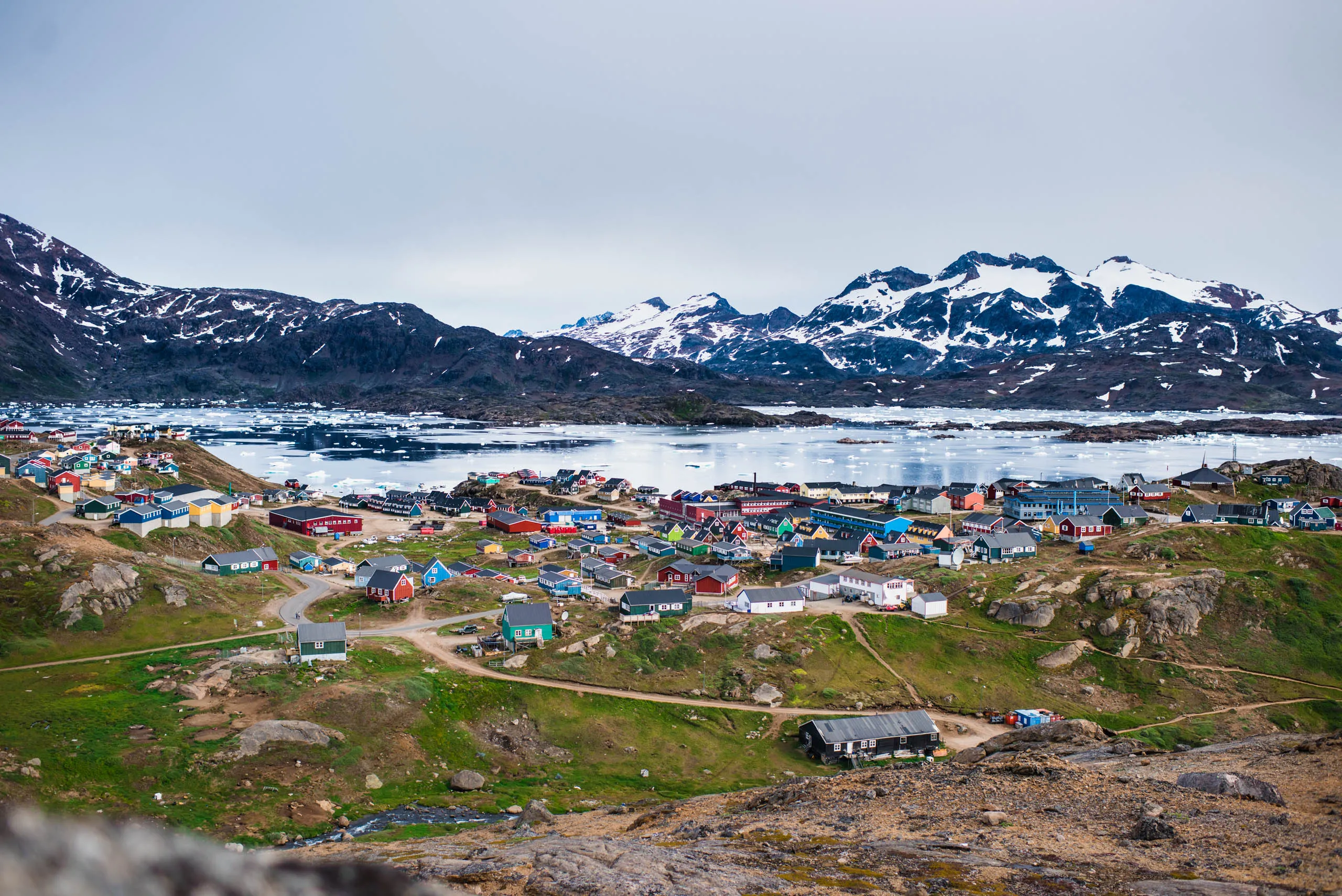 Panoramic view of a compact Arctic settlement spread across tundra beside an ice-filled harbour
