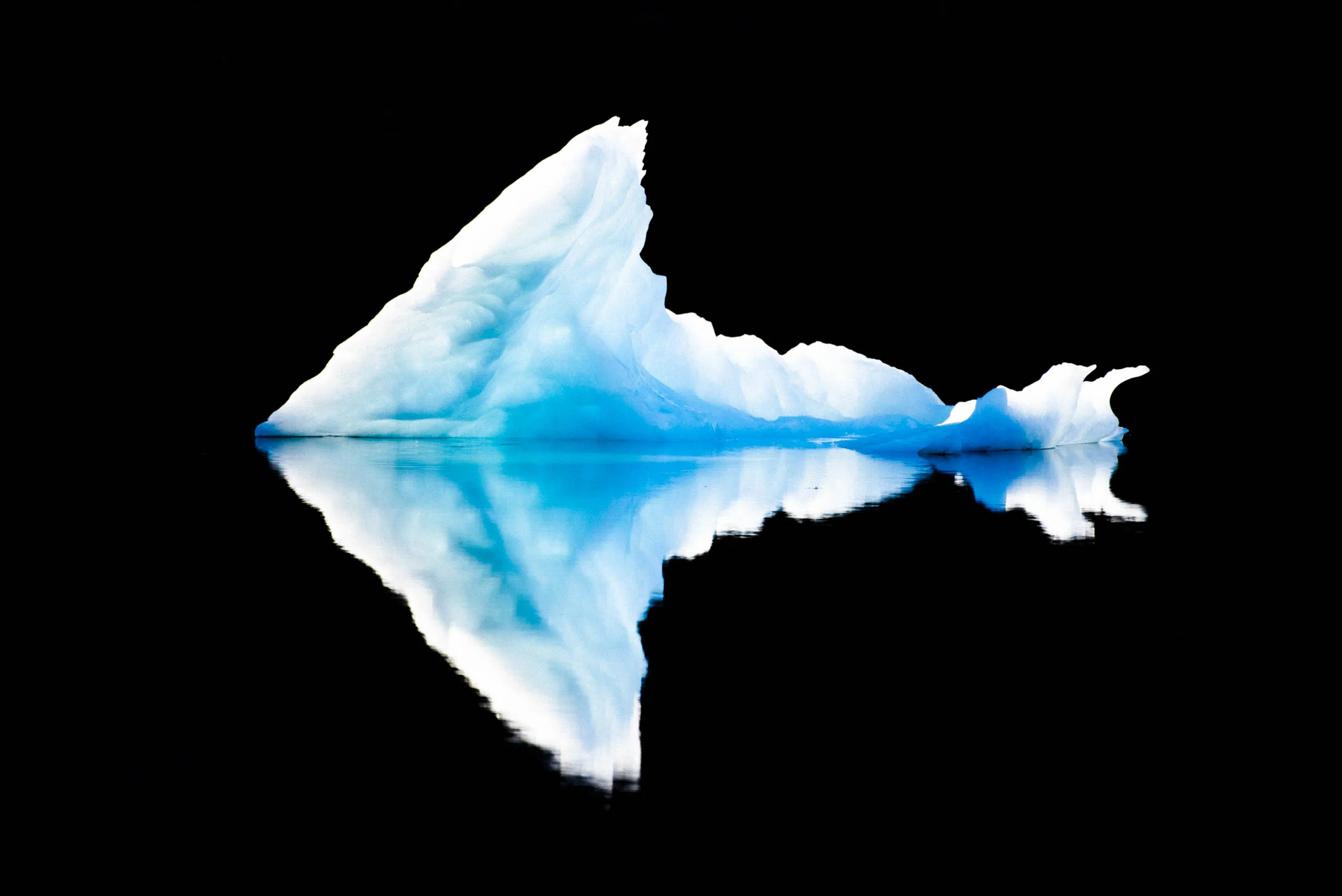Jagged blue iceberg shaped like a fin, mirrored symmetrically on a black fjord surface