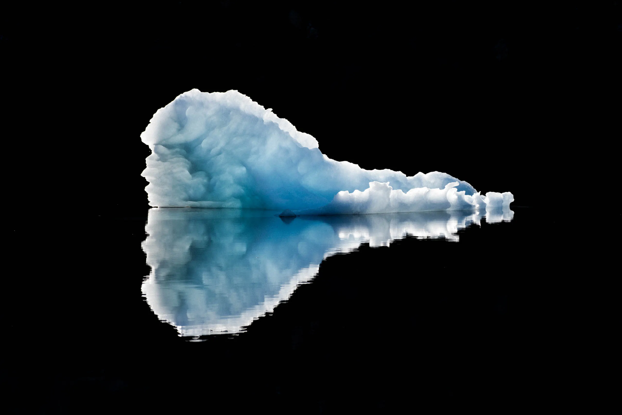 Glowing blue-white iceberg with a rounded crest mirrored perfectly in dark Arctic water