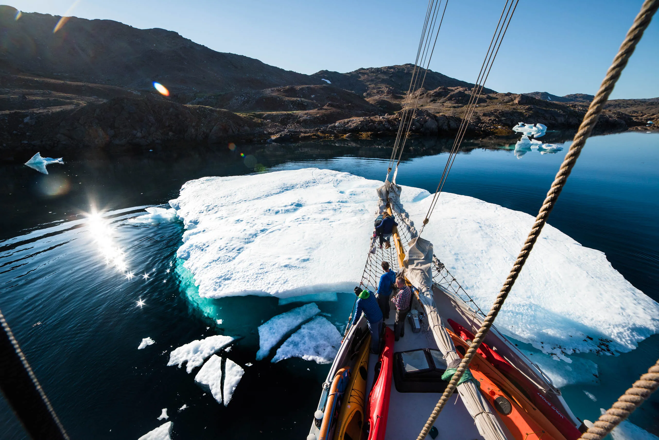 View from deck as the schooner noses close to a gleaming iceberg in a sunlit Arctic bay