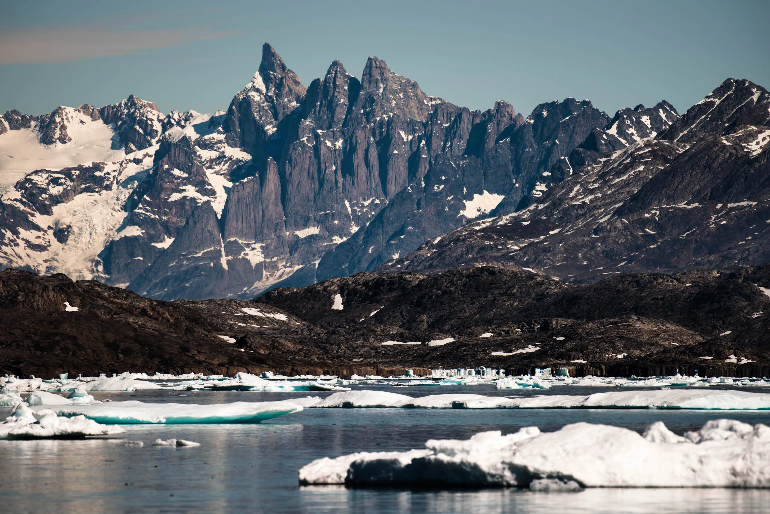 Jagged granite peaks rise steeply above a fjord scattered with drifting sea ice