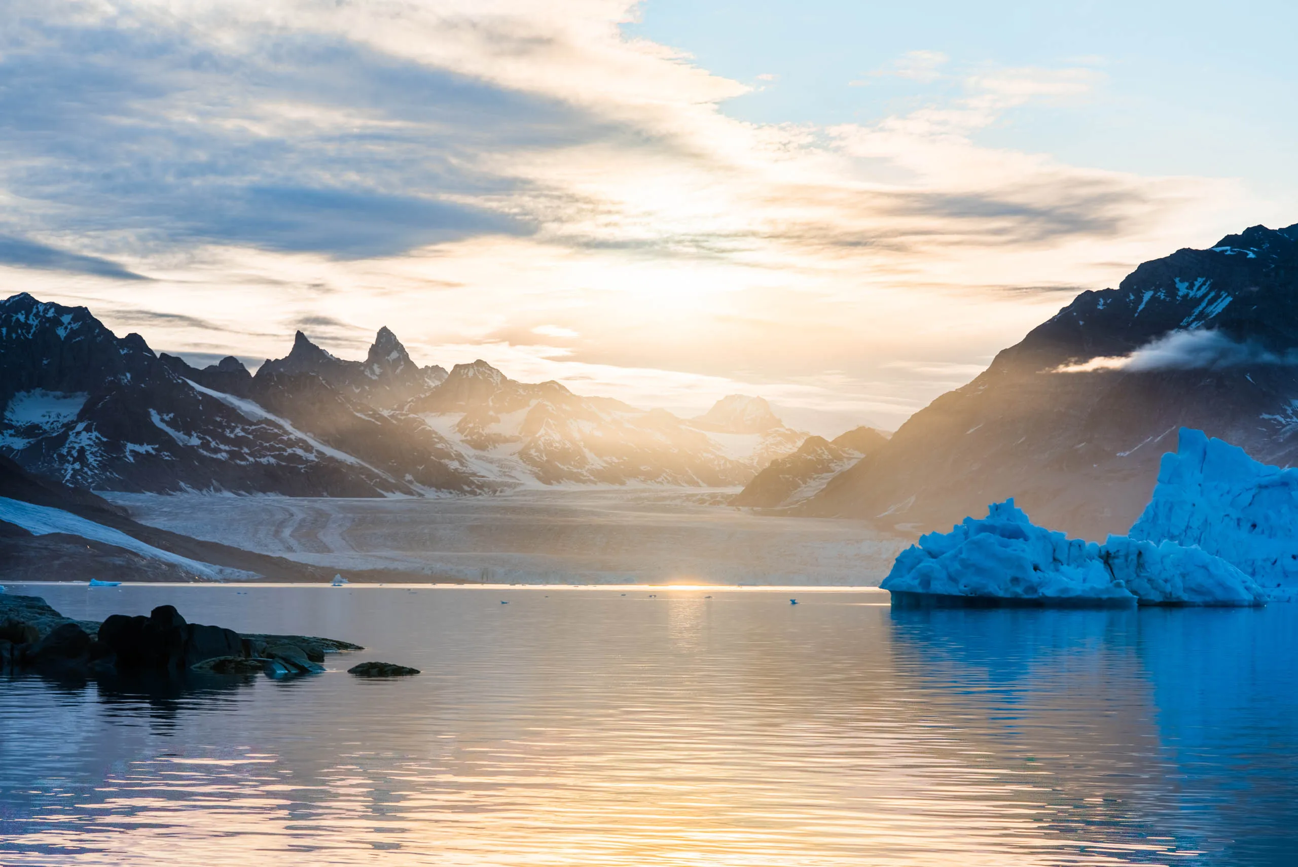 Midnight sun glows golden over a glacier and fjord beside a massive blue iceberg