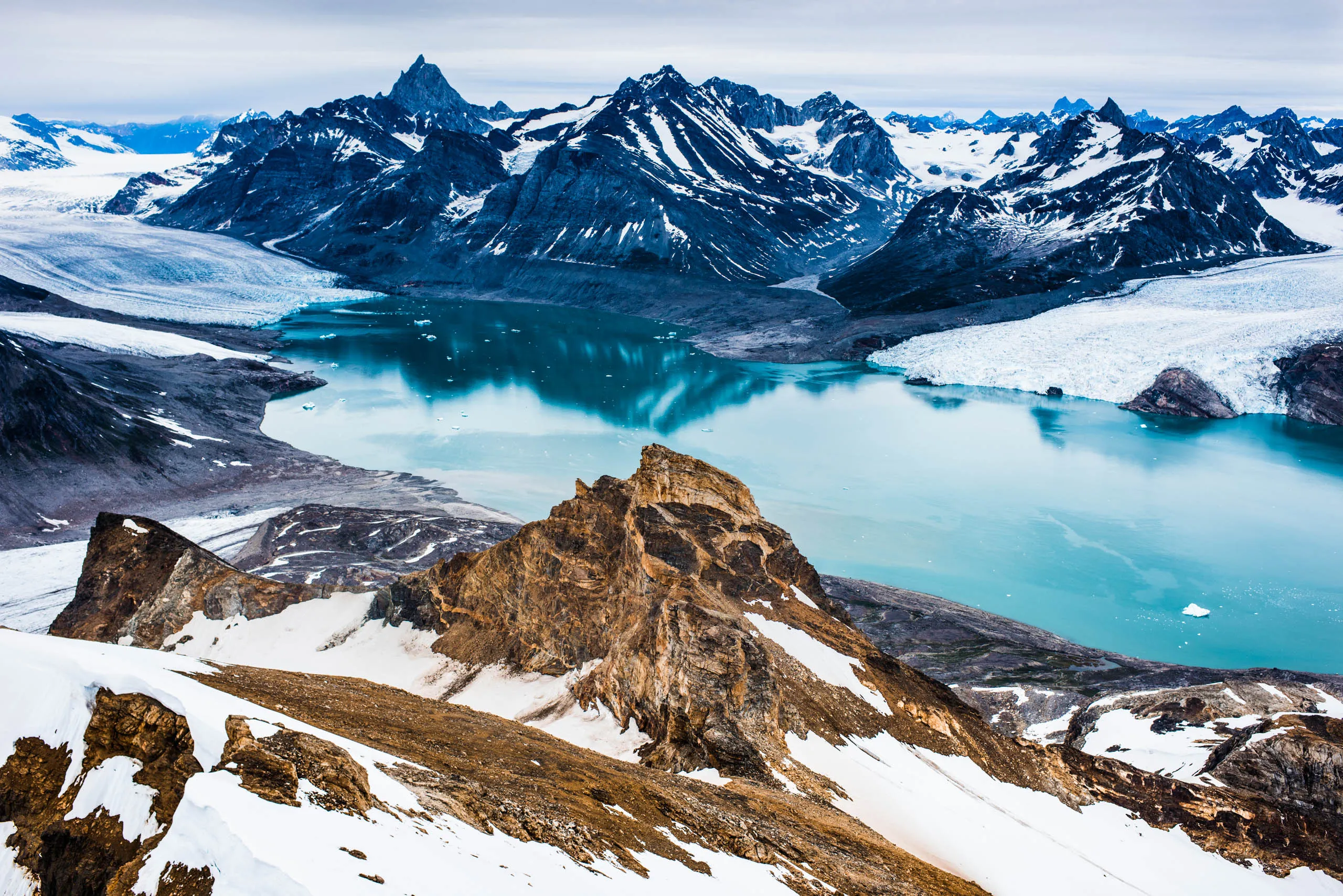 Aerial view of a turquoise glacial fjord flanked by snow-covered peaks in East Greenland