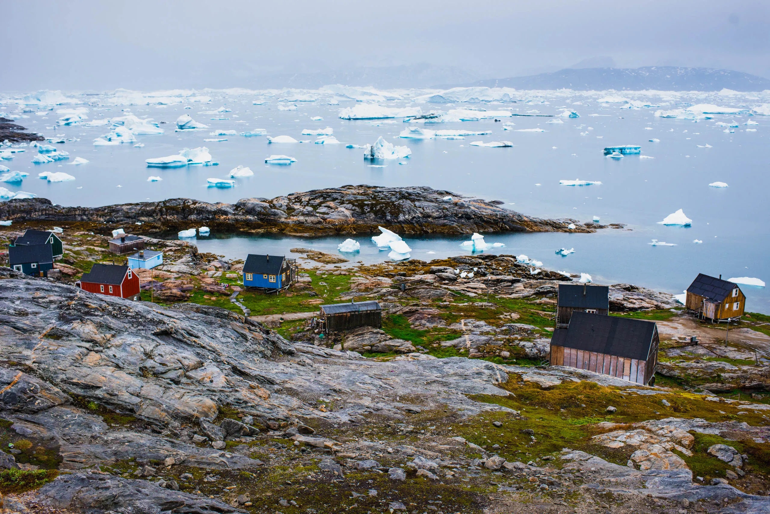 Colourful wooden houses of a remote Greenlandic settlement overlooking an iceberg-strewn bay