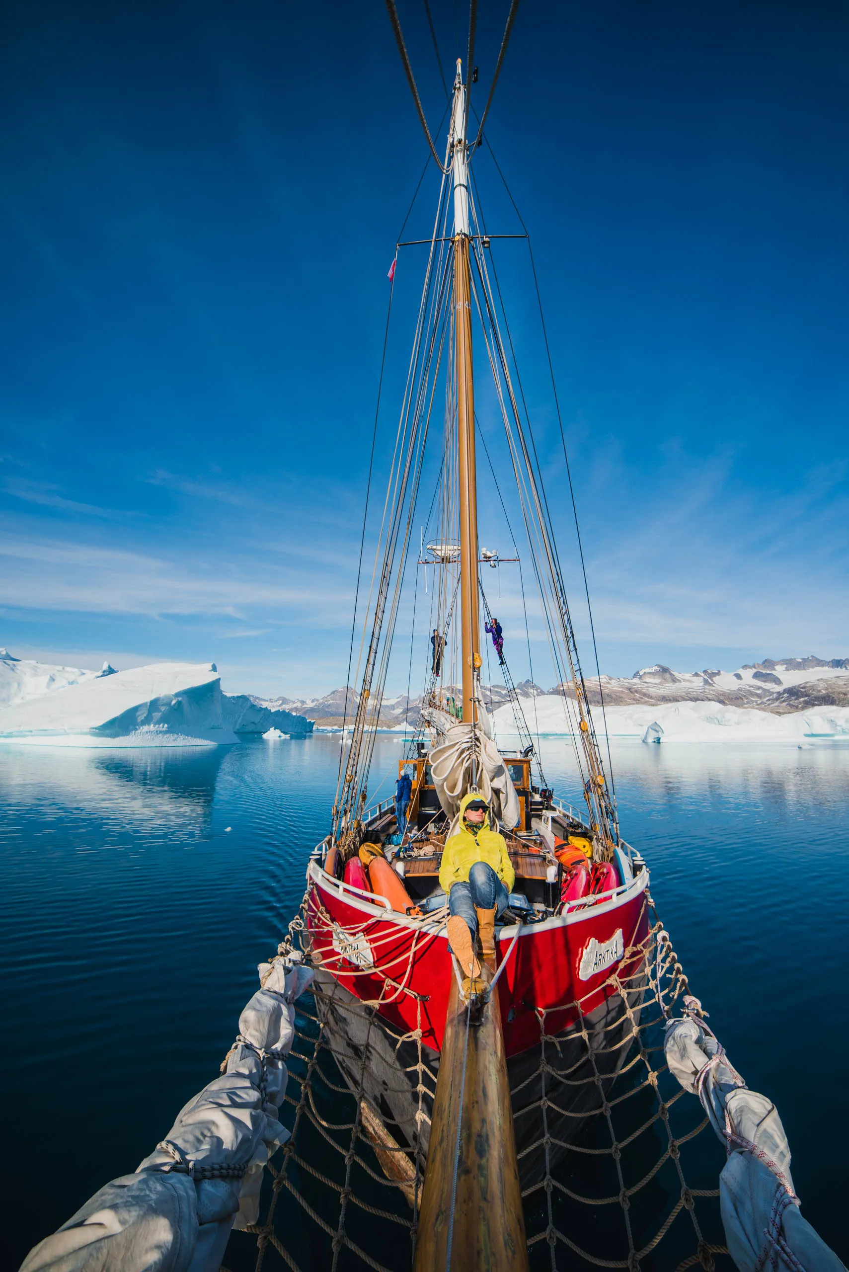 View from the bowsprit of Aurora Arktika sailing through a sunlit fjord lined with icebergs