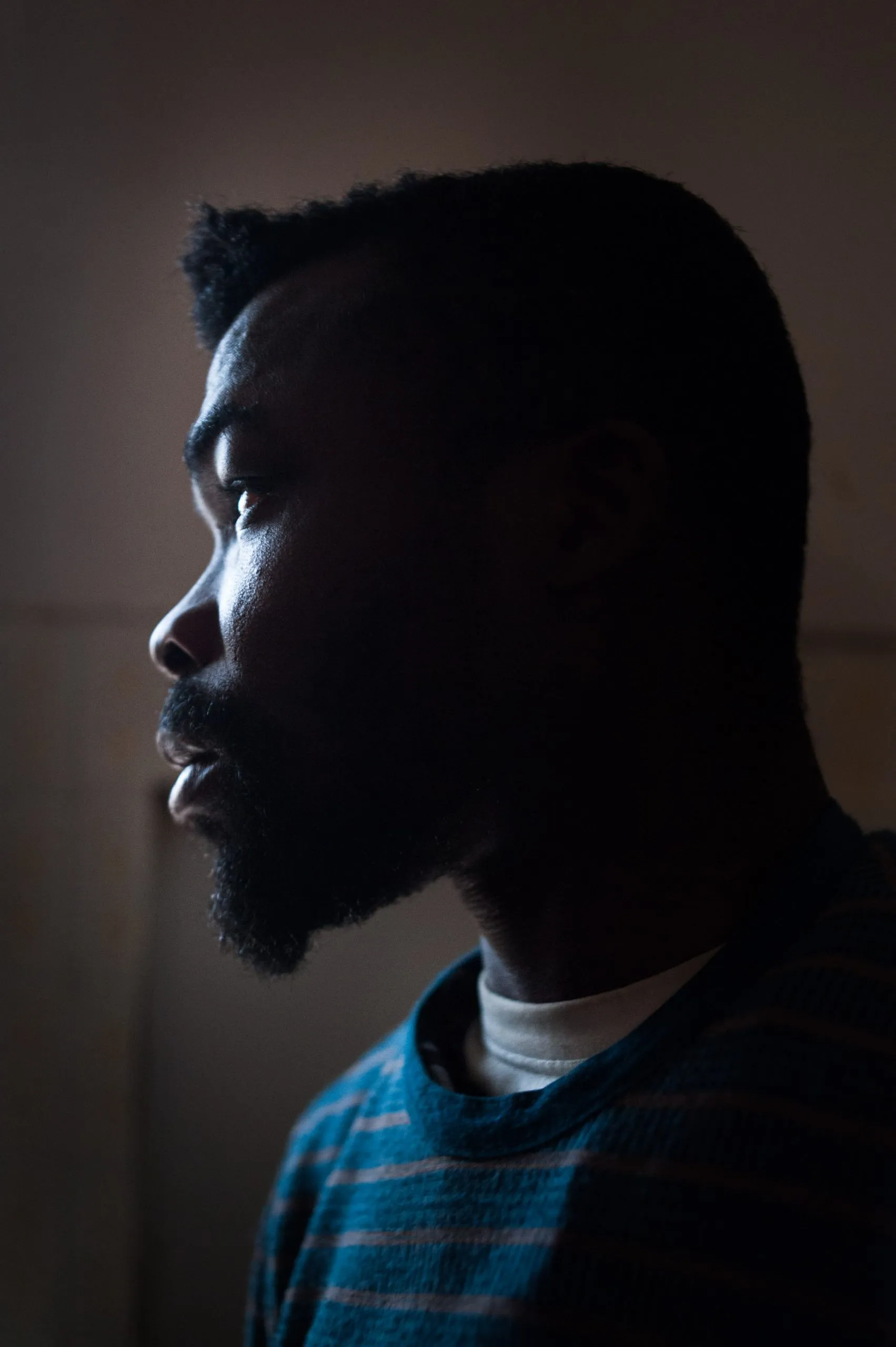 A bearded man's profile against a bare wall in low light, inside the disused warehouse in Rosarno, Calabria.
