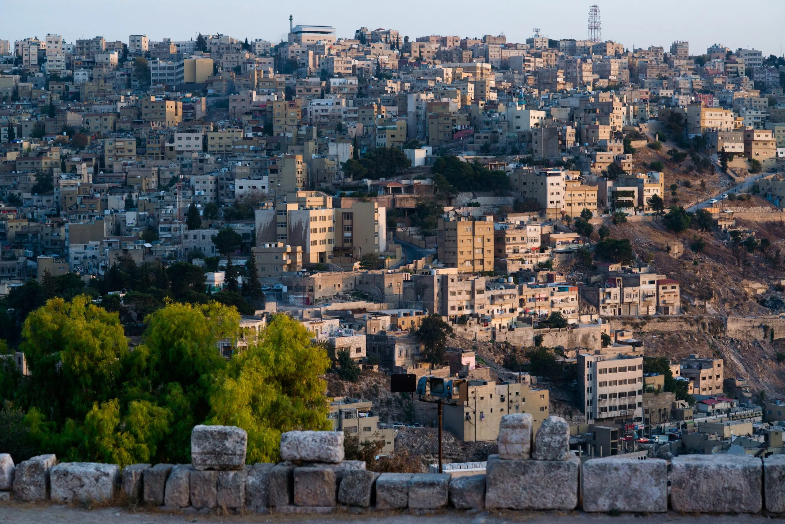 An evening view across the dense, tan-coloured hillside neighbourhoods of Amman, Jordan.