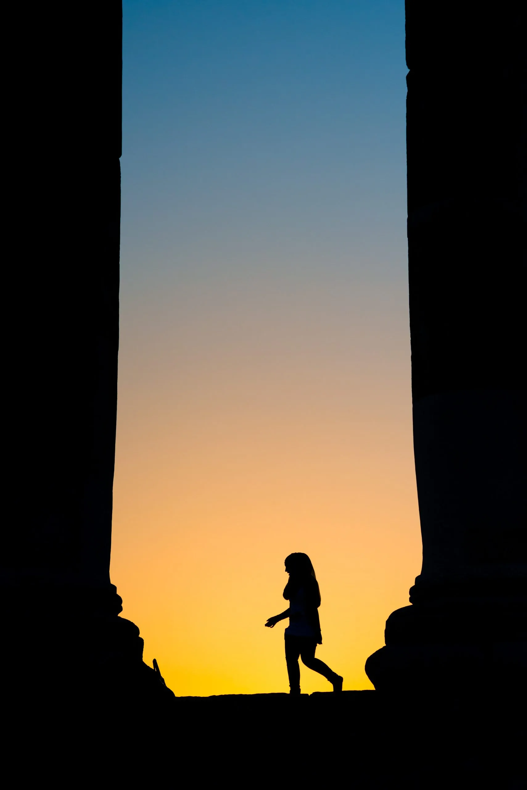 A woman walks between massive Roman columns silhouetted against a deep gold-and-blue sunset, at Jerash, Jordan.