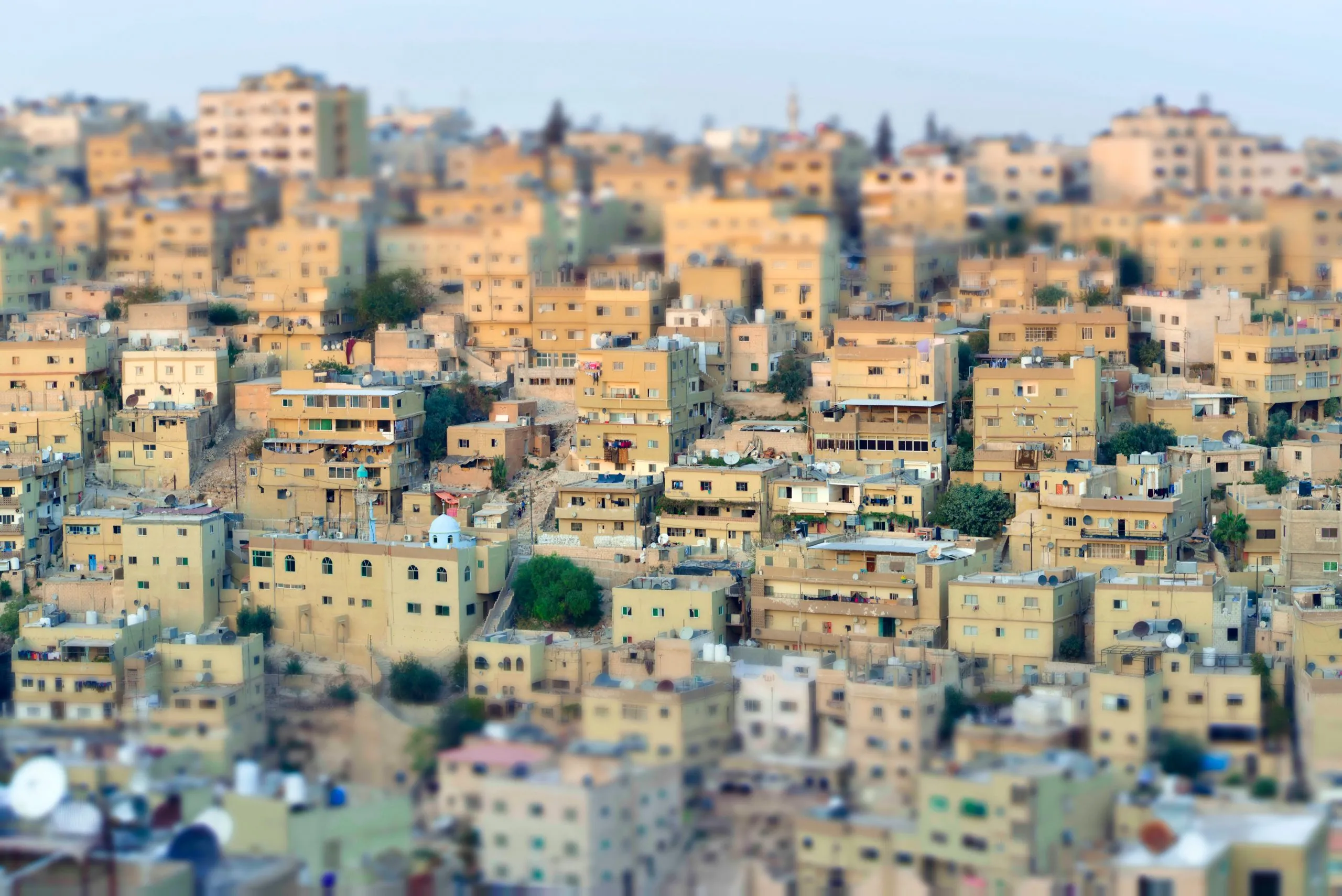 Tilt-shift view of the dense beige buildings climbing the hills of Amman, Jordan.
