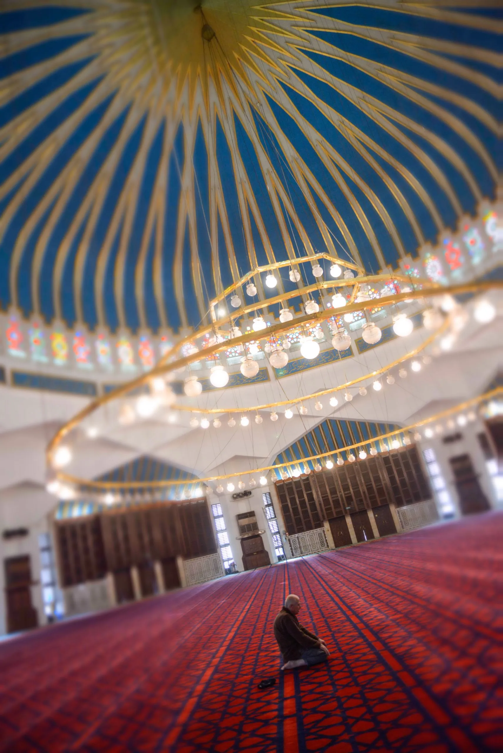 A single figure prays beneath the painted blue dome of the King Abdullah Mosque in Amman, Jordan.