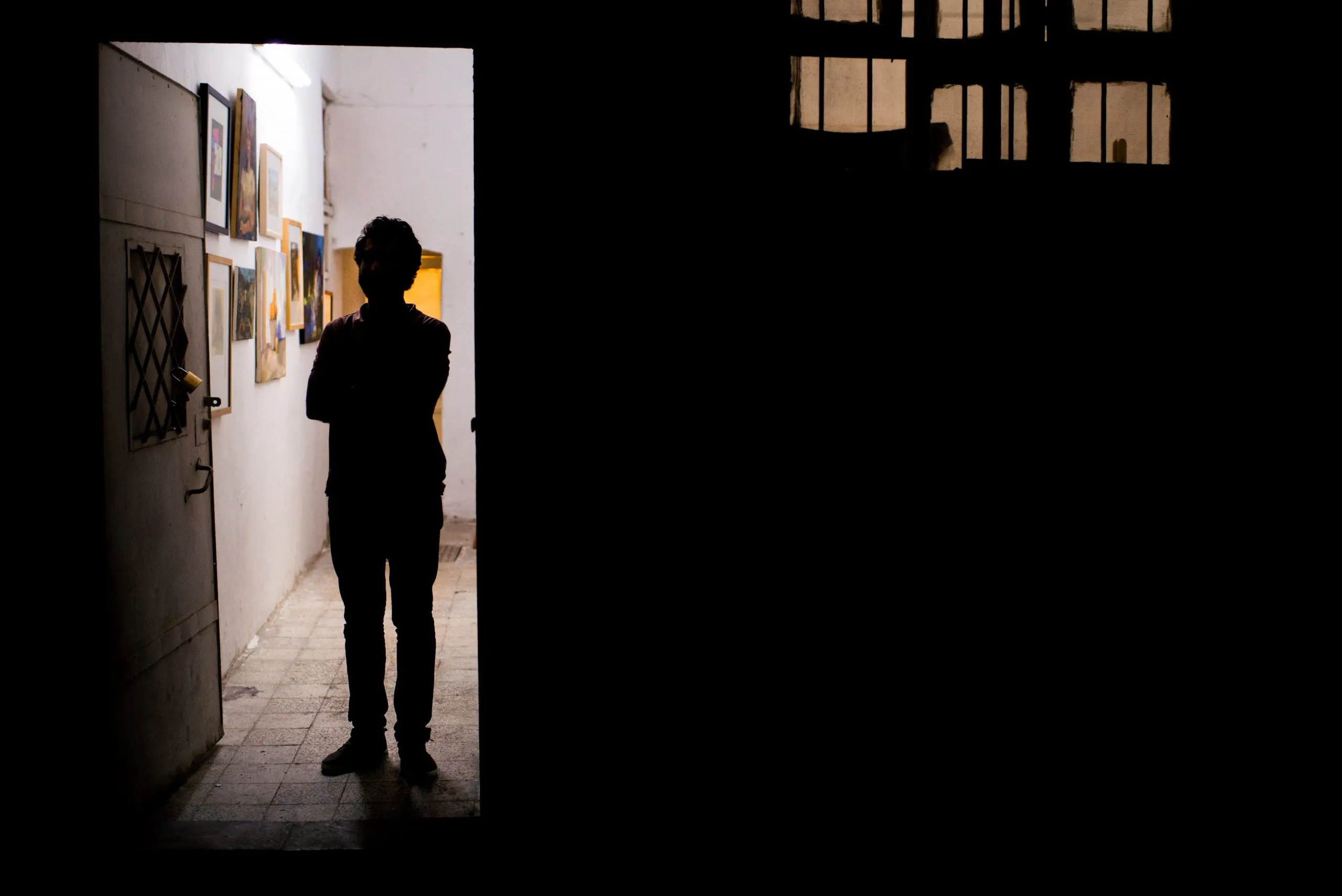 A silhouetted figure stands in a doorway of an art gallery hung with paintings, in Amman.