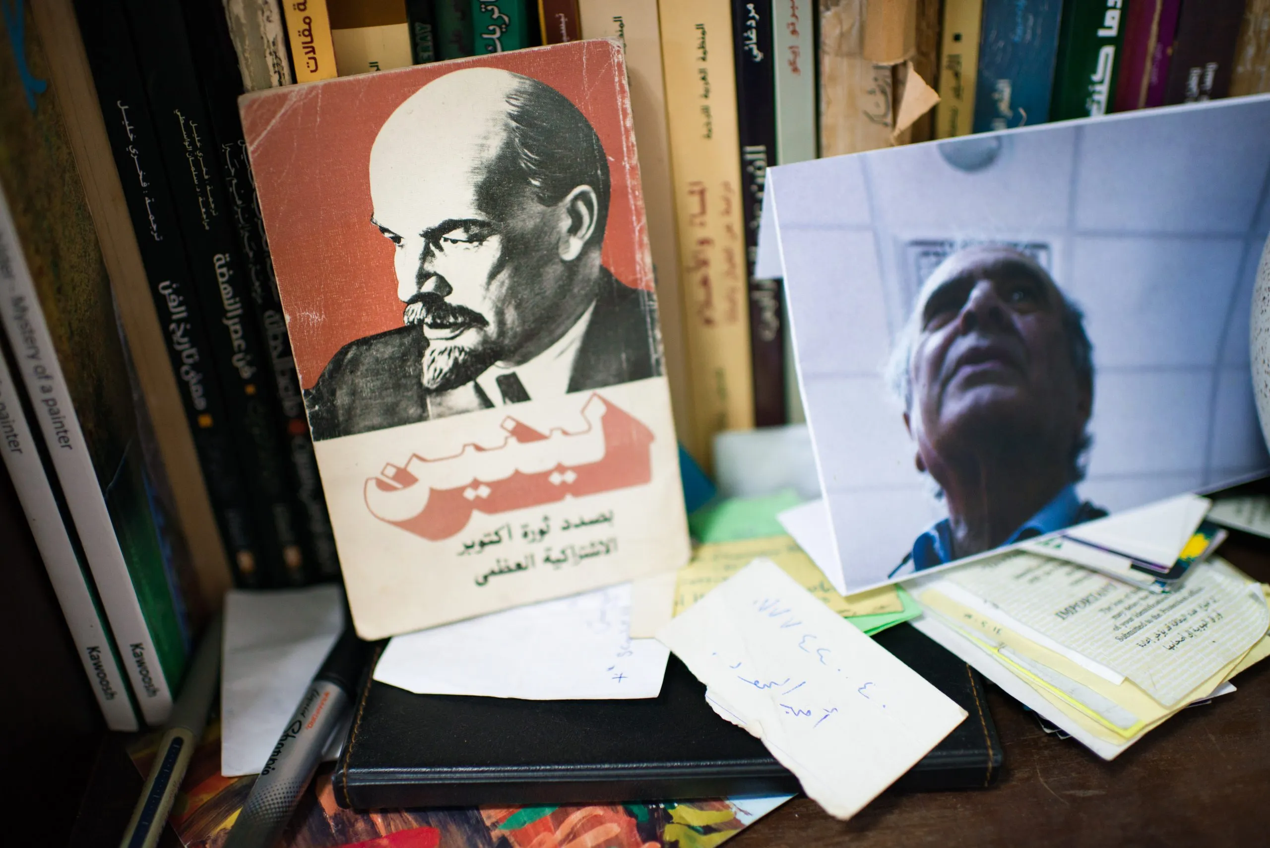 An Arabic-language book about Lenin and a black-and-white photograph of an older man, on a cluttered desk.