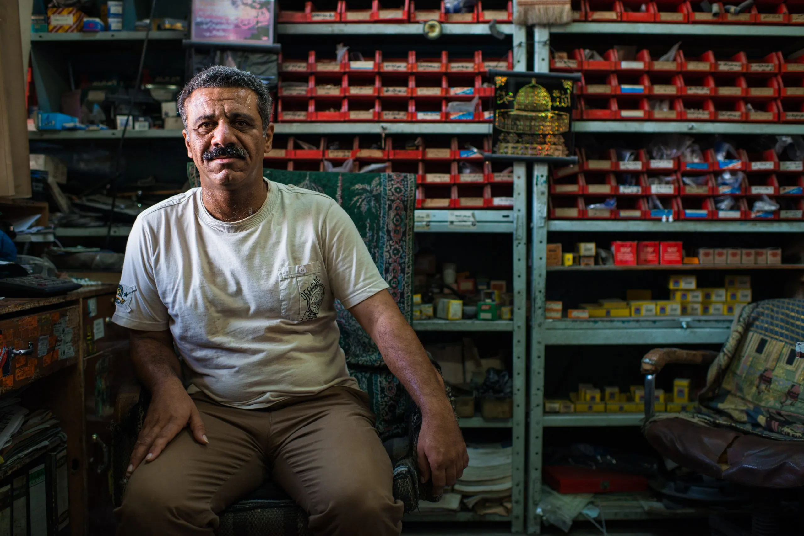 A shopkeeper sits among shelves stocked with hundreds of small car parts in an Amman repair shop.