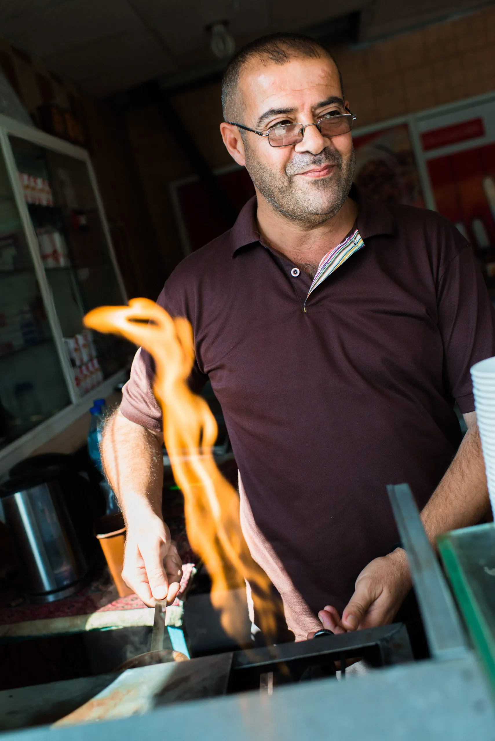 A café cook tends a tall flame from a gas griddle inside his small shop in Amman, Jordan.