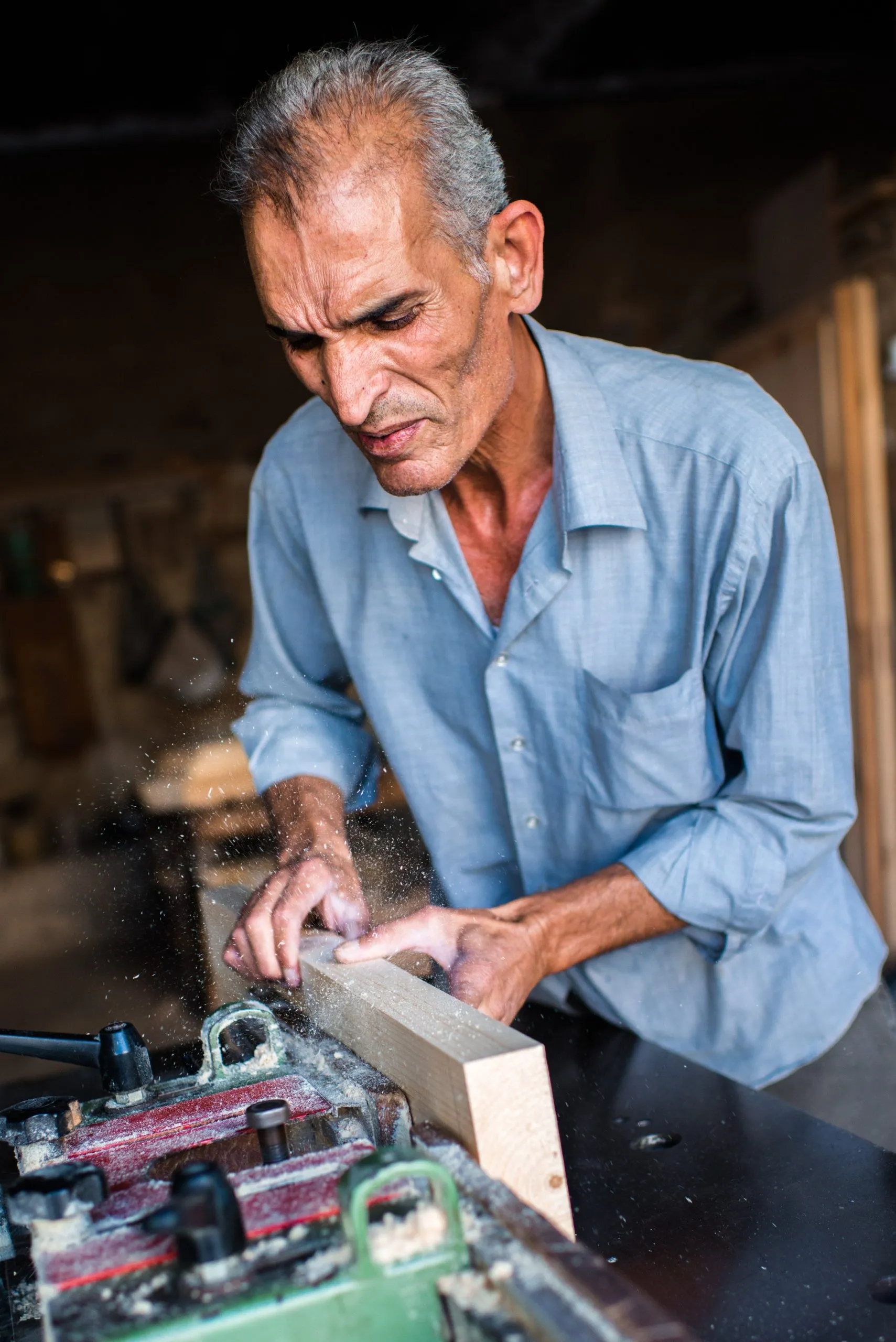A carpenter feeds a wooden board into a small sanding machine in his workshop in Amman.