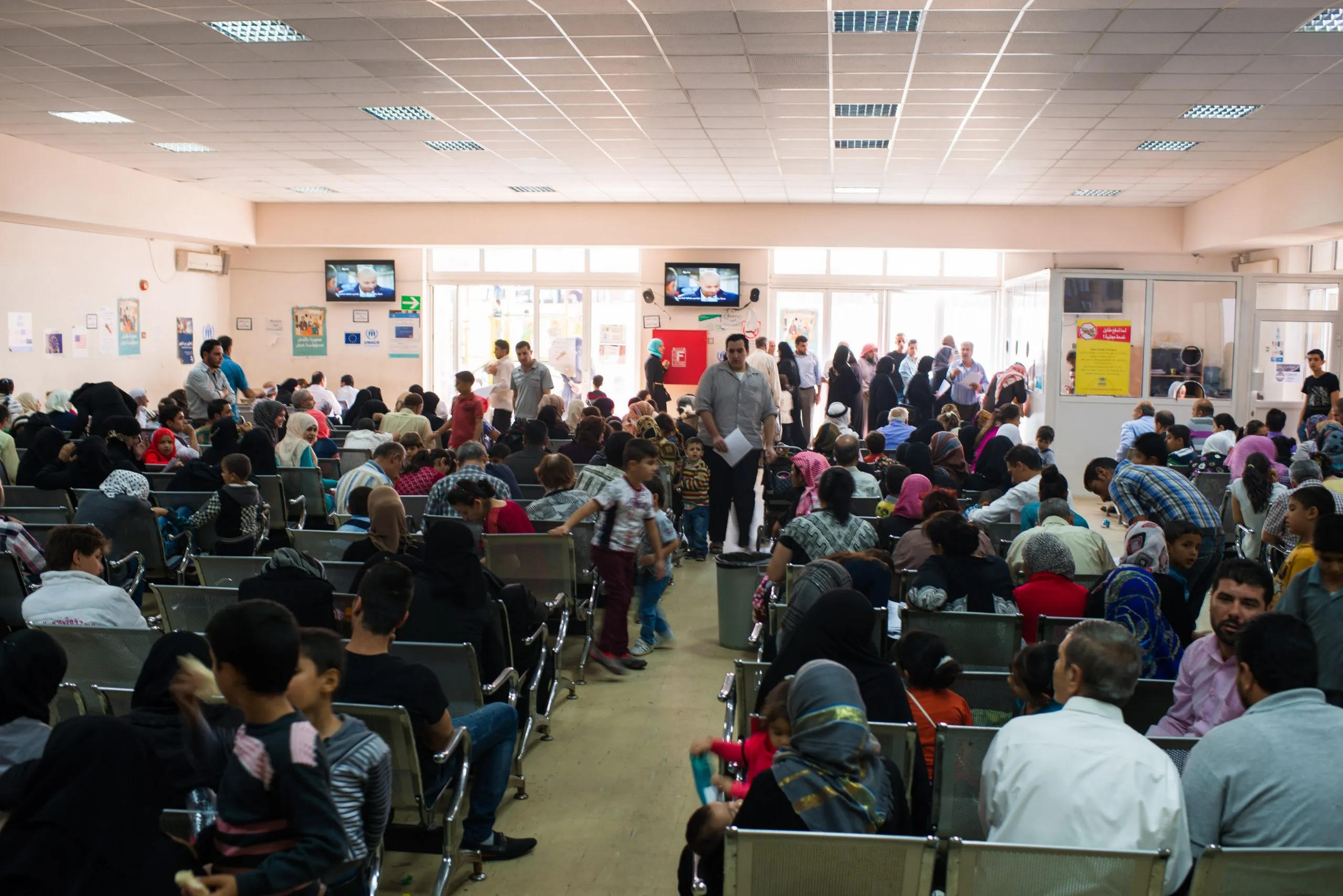 A crowded waiting room at a UN registration centre in Jordan, with rows of people of all ages on plastic seats.