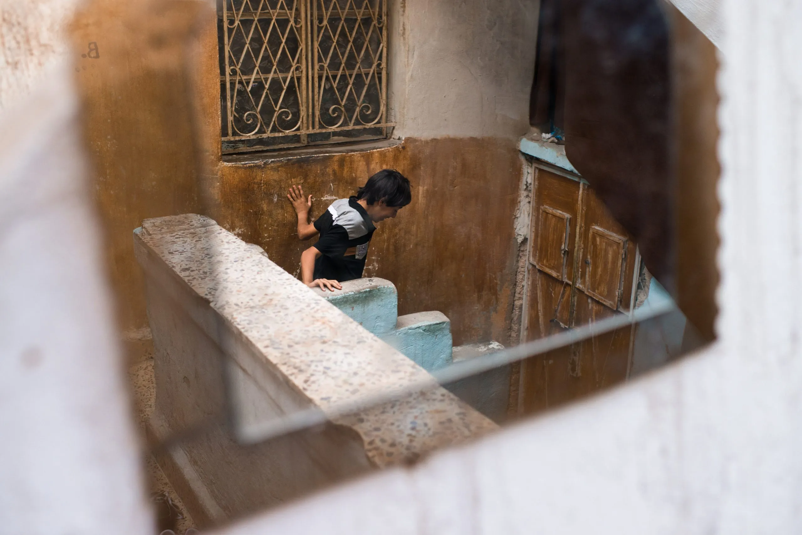 Reflection through a dusty mirror of a boy climbing a small terracotta stair in an Amman alleyway.