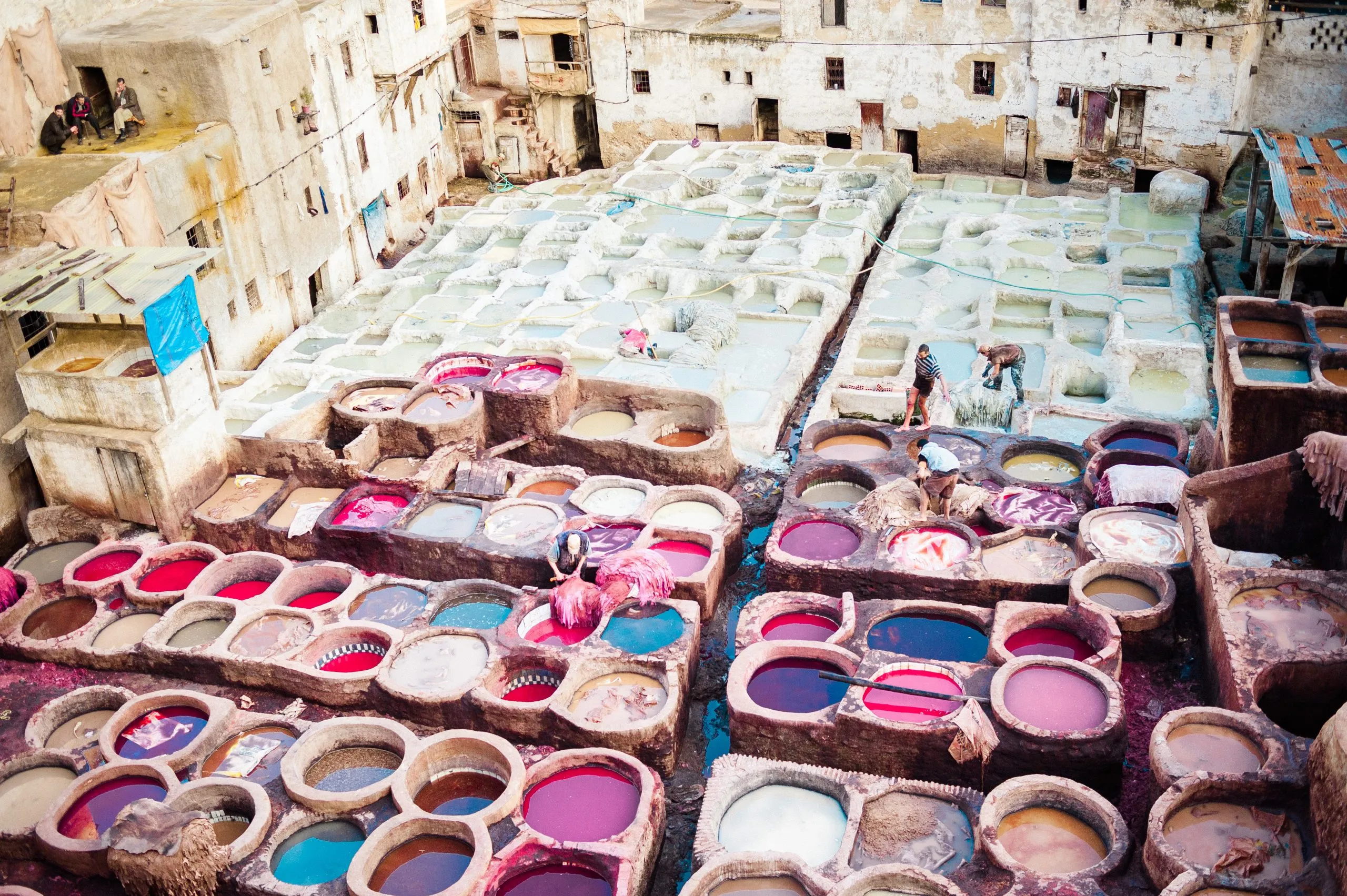Aerial view of the Chouara tannery in Fez, Morocco — circular vats of red, blue and white dye packed into the medina, workers and drying skins among them.