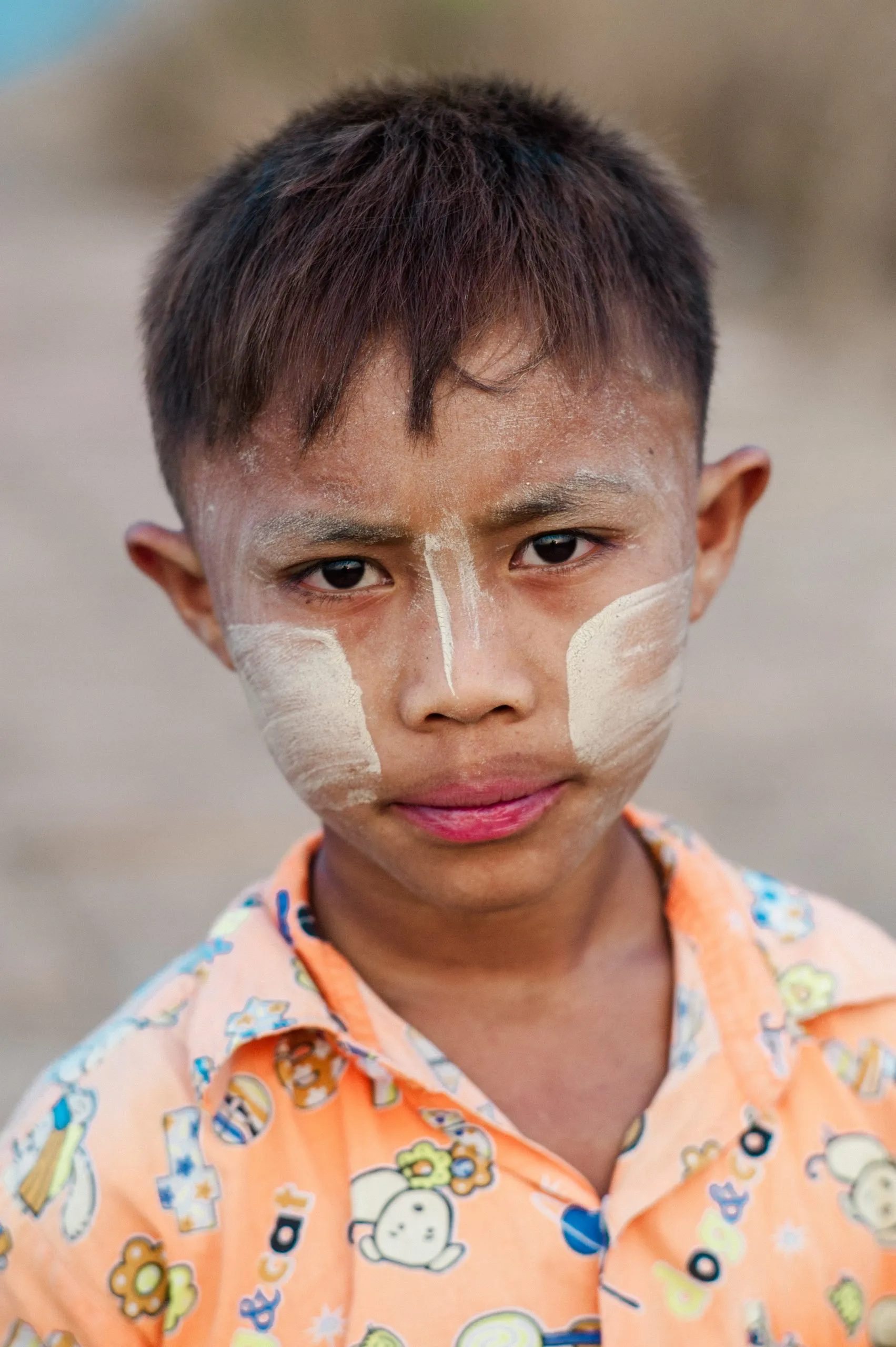 A close portrait of a Burmese boy with traditional thanaka paste painted on his cheeks and nose.
