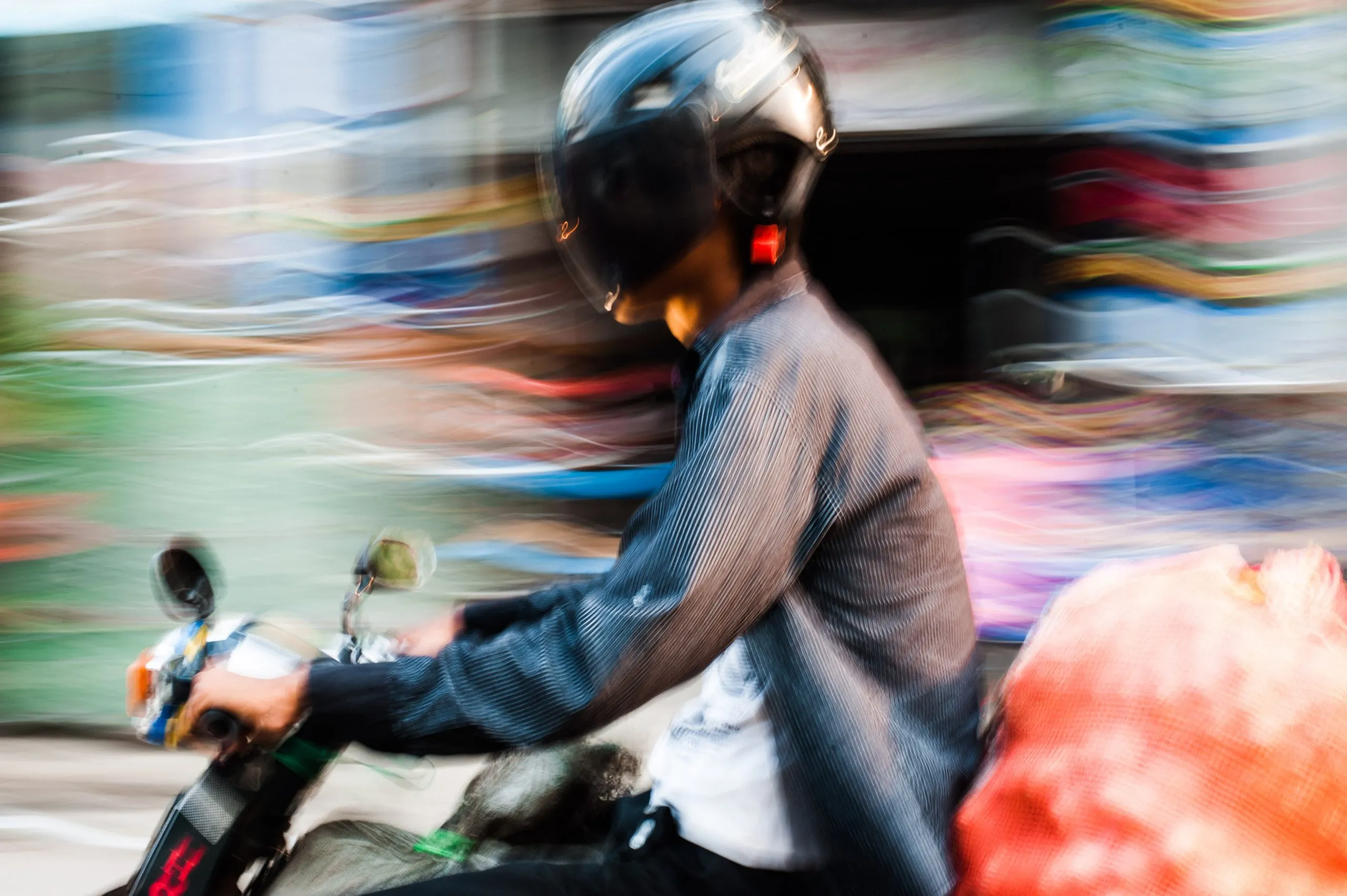 A helmeted motorcyclist photographed in motion blur against the colours of a Burmese street.