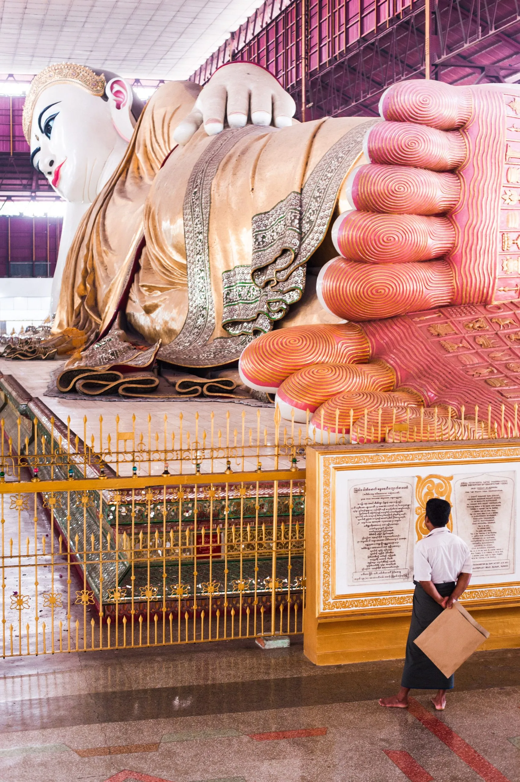 A man stands beside the giant reclining Buddha at Chaukhtatgyi temple in Yangon, its painted soles facing the camera.