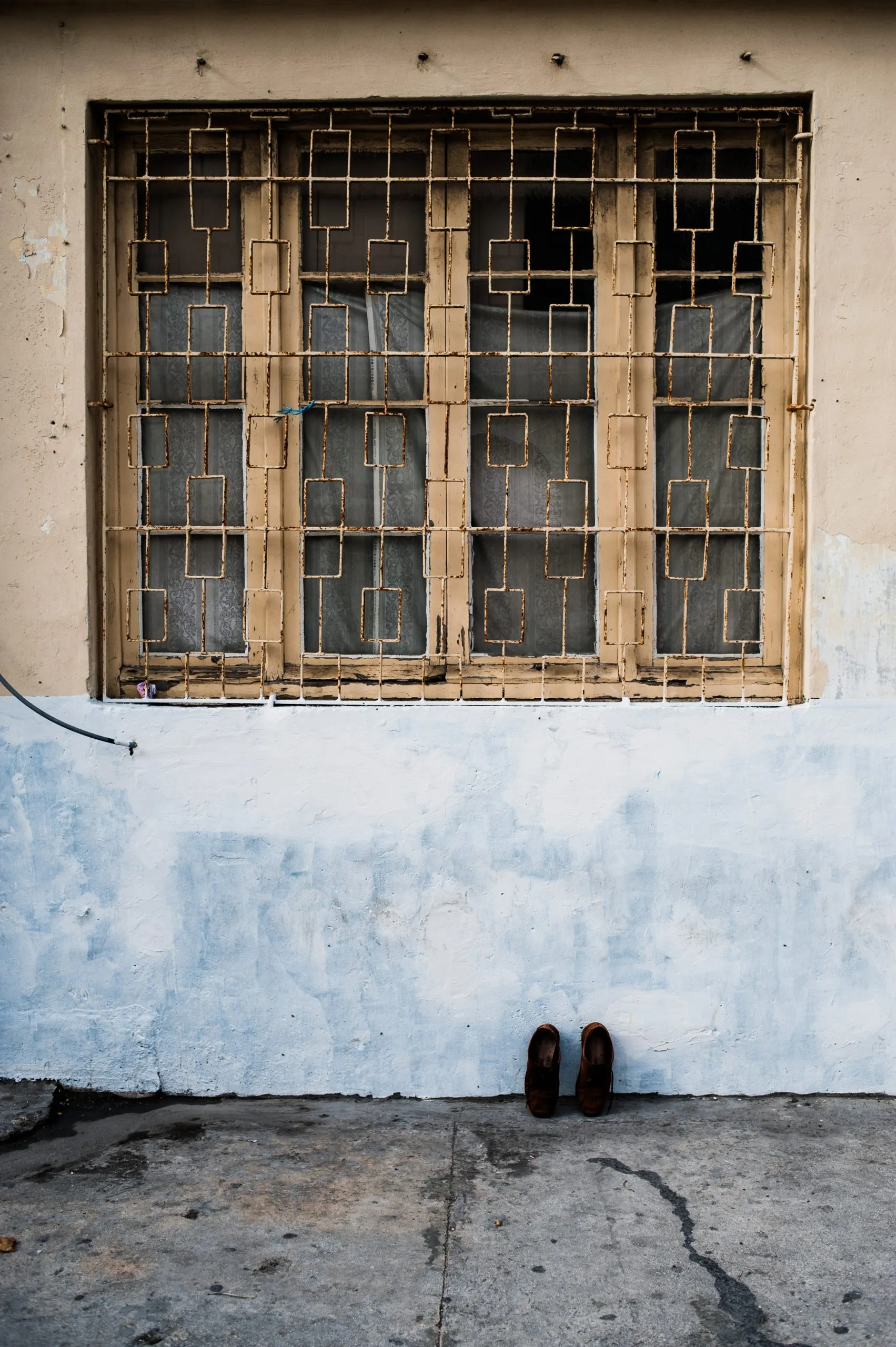 A pair of leather shoes left below a barred and decoratively grilled window on a Maltese street.