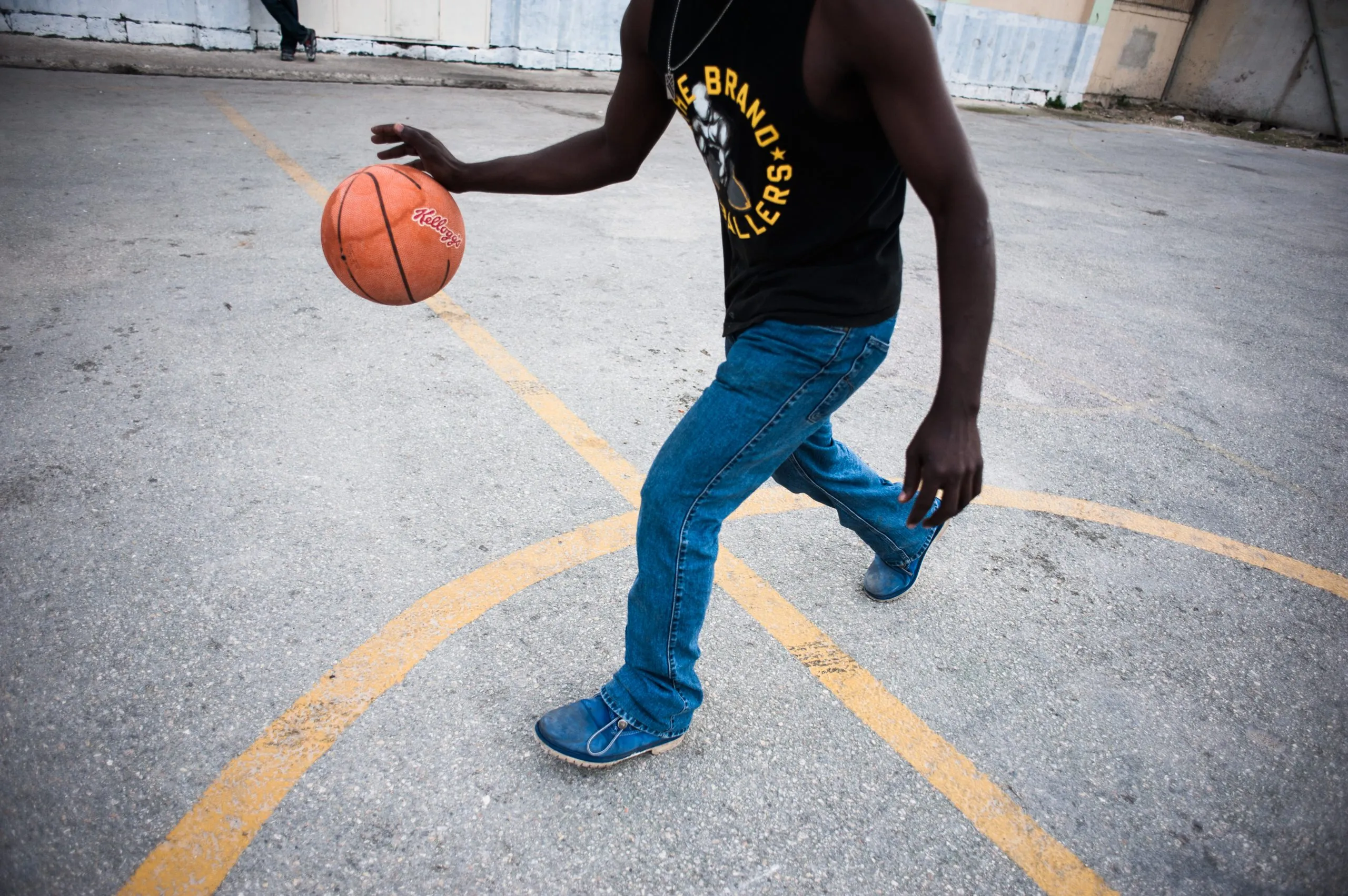 A man dribbling a basketball on a worn outdoor court at the Malta housing compound.