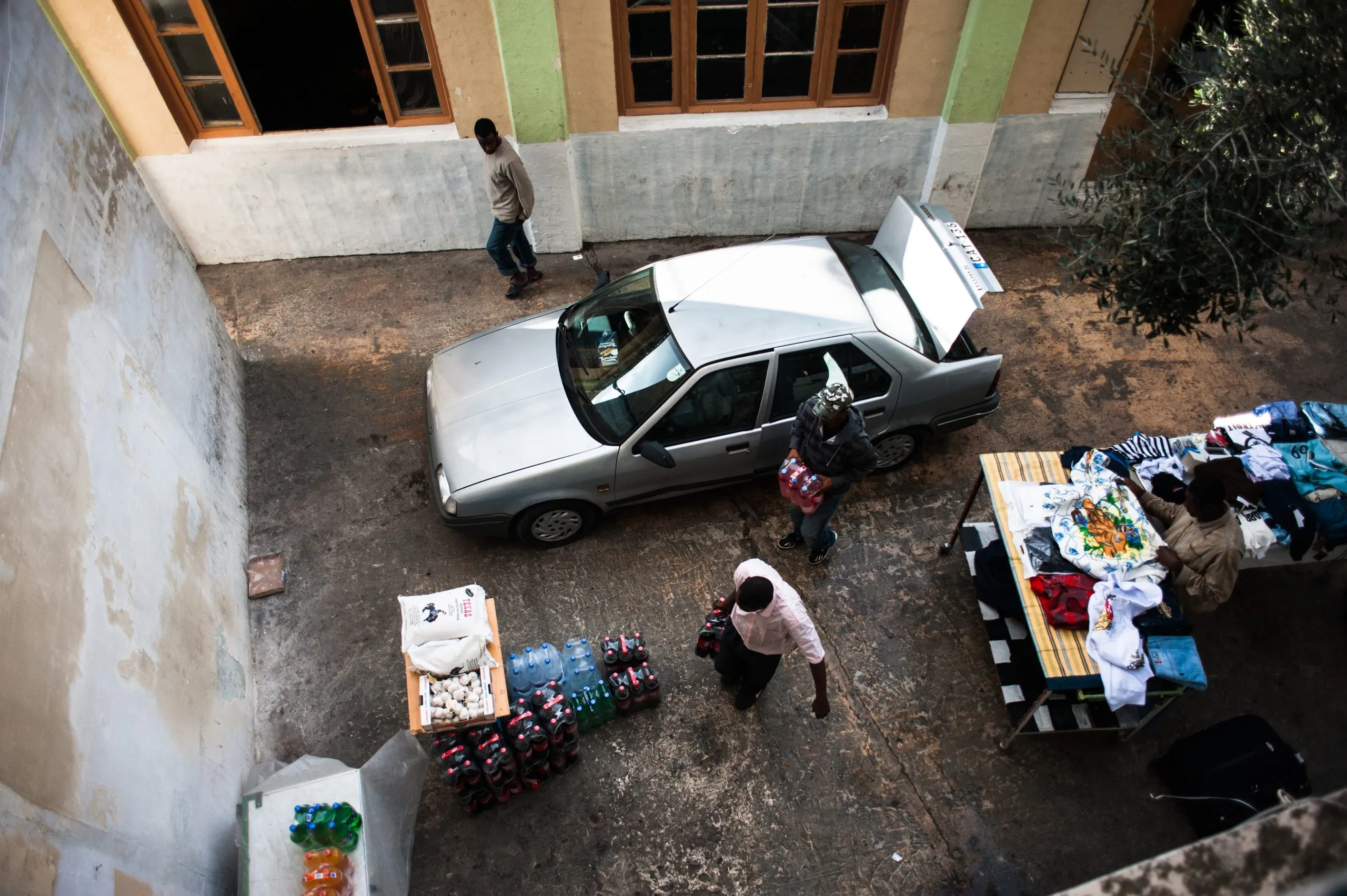 Looking down on a parked car beside a clothing-and-goods stall in the courtyard of the Malta compound.