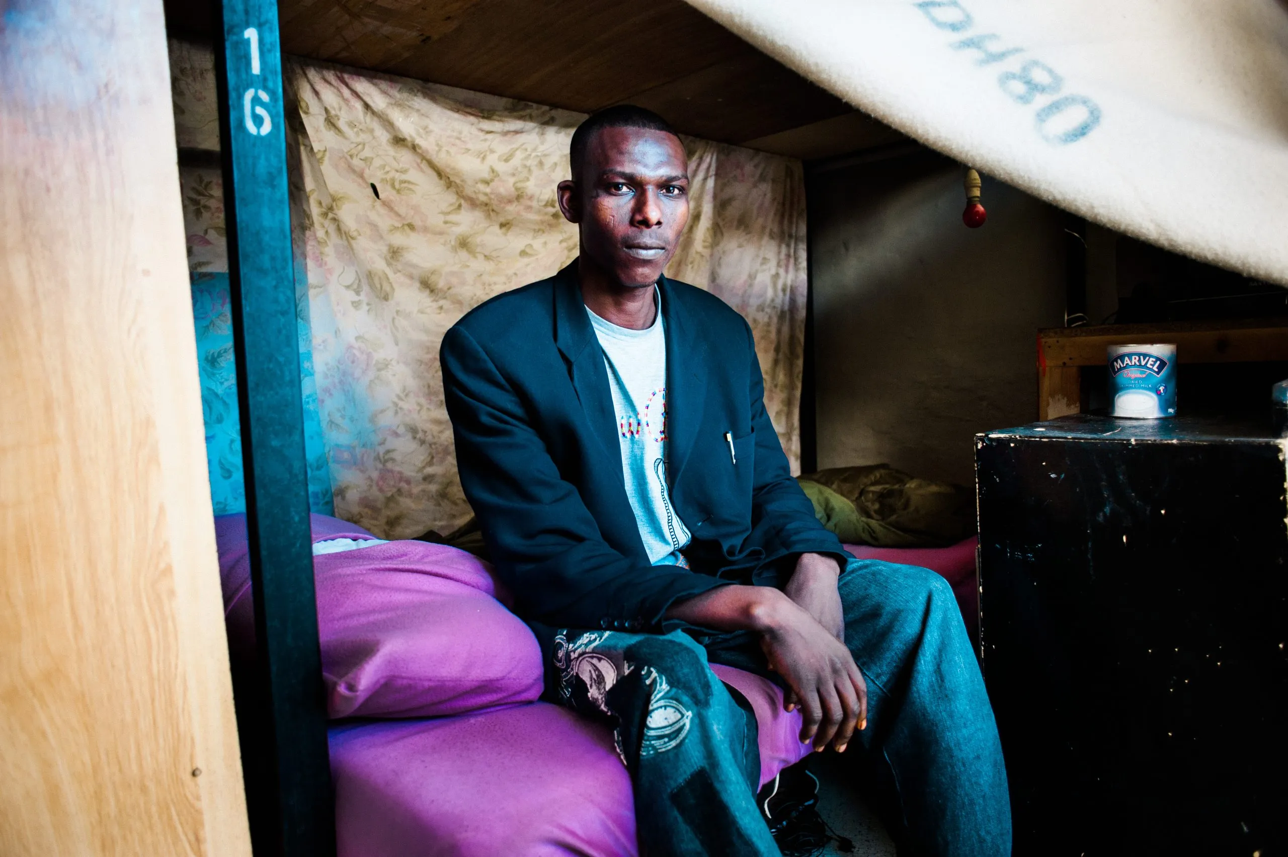 A man sits on bunk number 16 inside his curtained sleeping space in the Malta hangar housing.