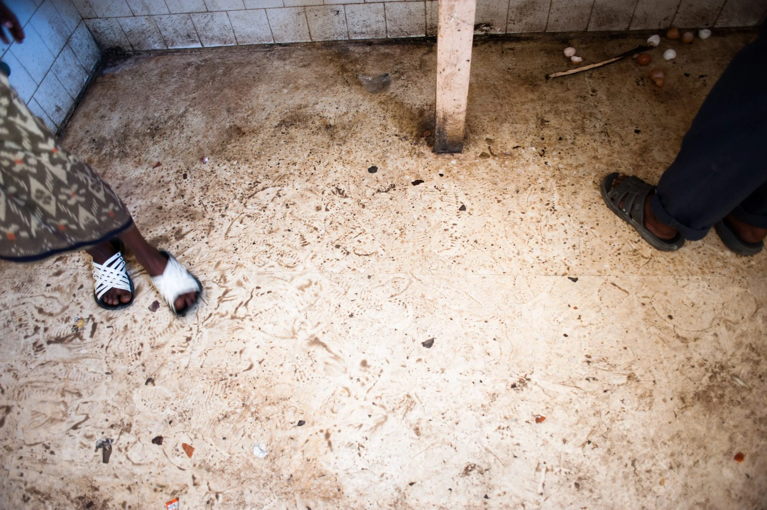 Sandals and bare feet beside spilled sand and footprints on the tiled floor of the Malta housing hangar.