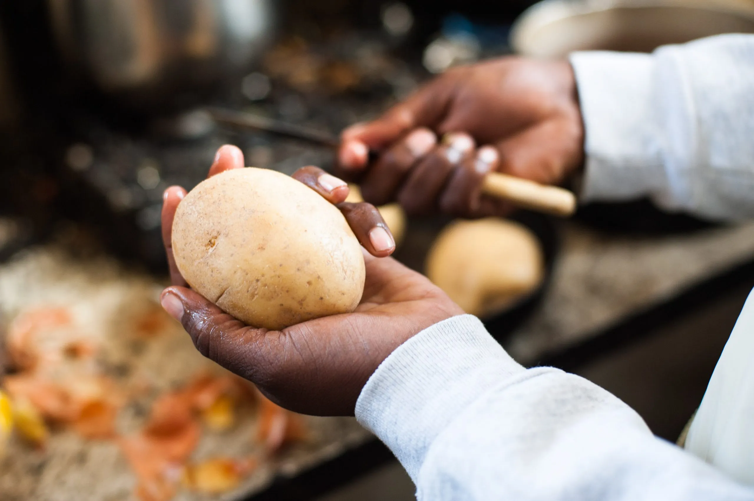 Hands hold and peel a potato over a kitchen surface in the shared kitchen of the Malta housing compound.