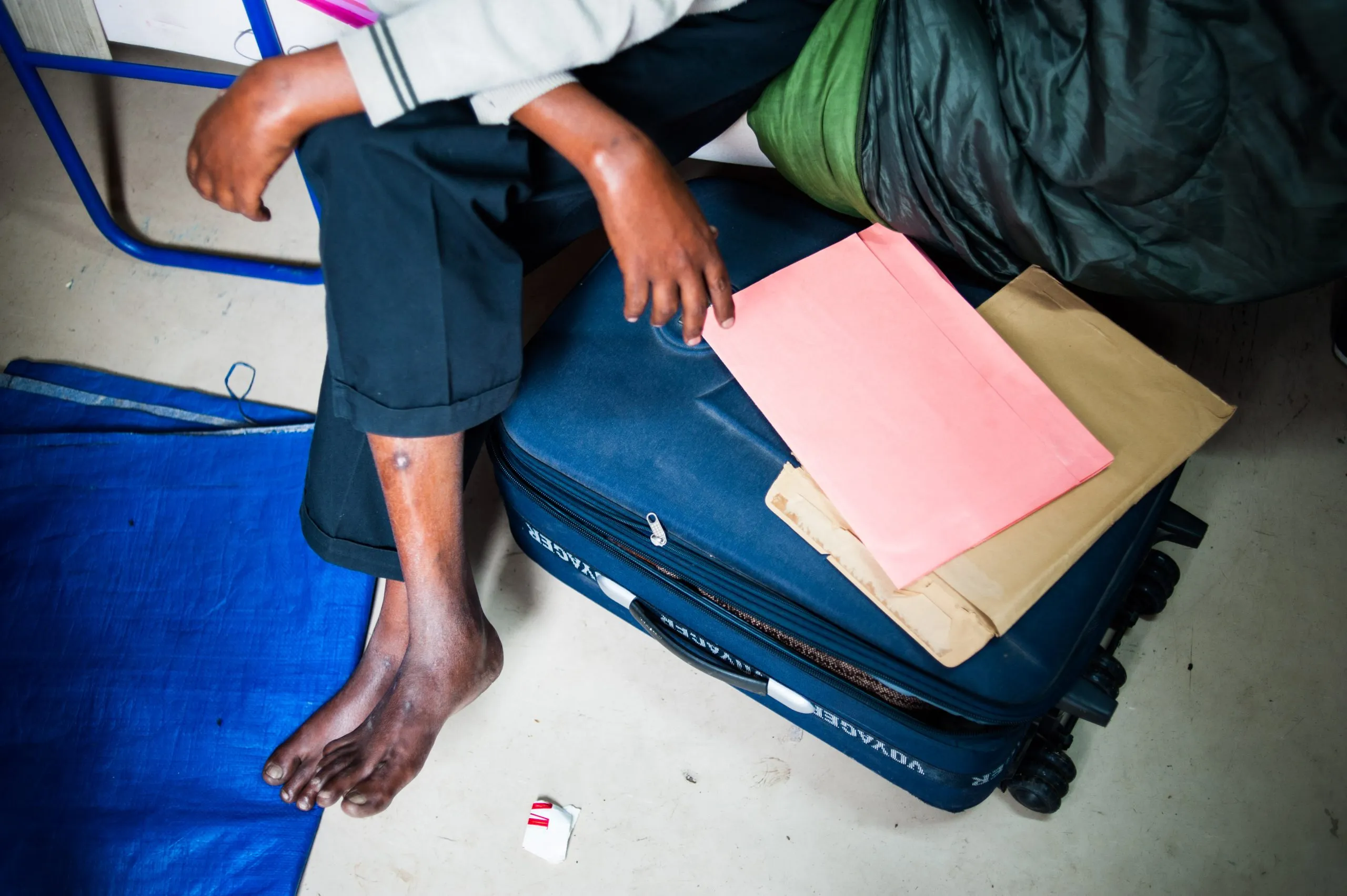 A person sits on a wheeled suitcase, with paperwork on its lid, inside the hangar housing on Malta.