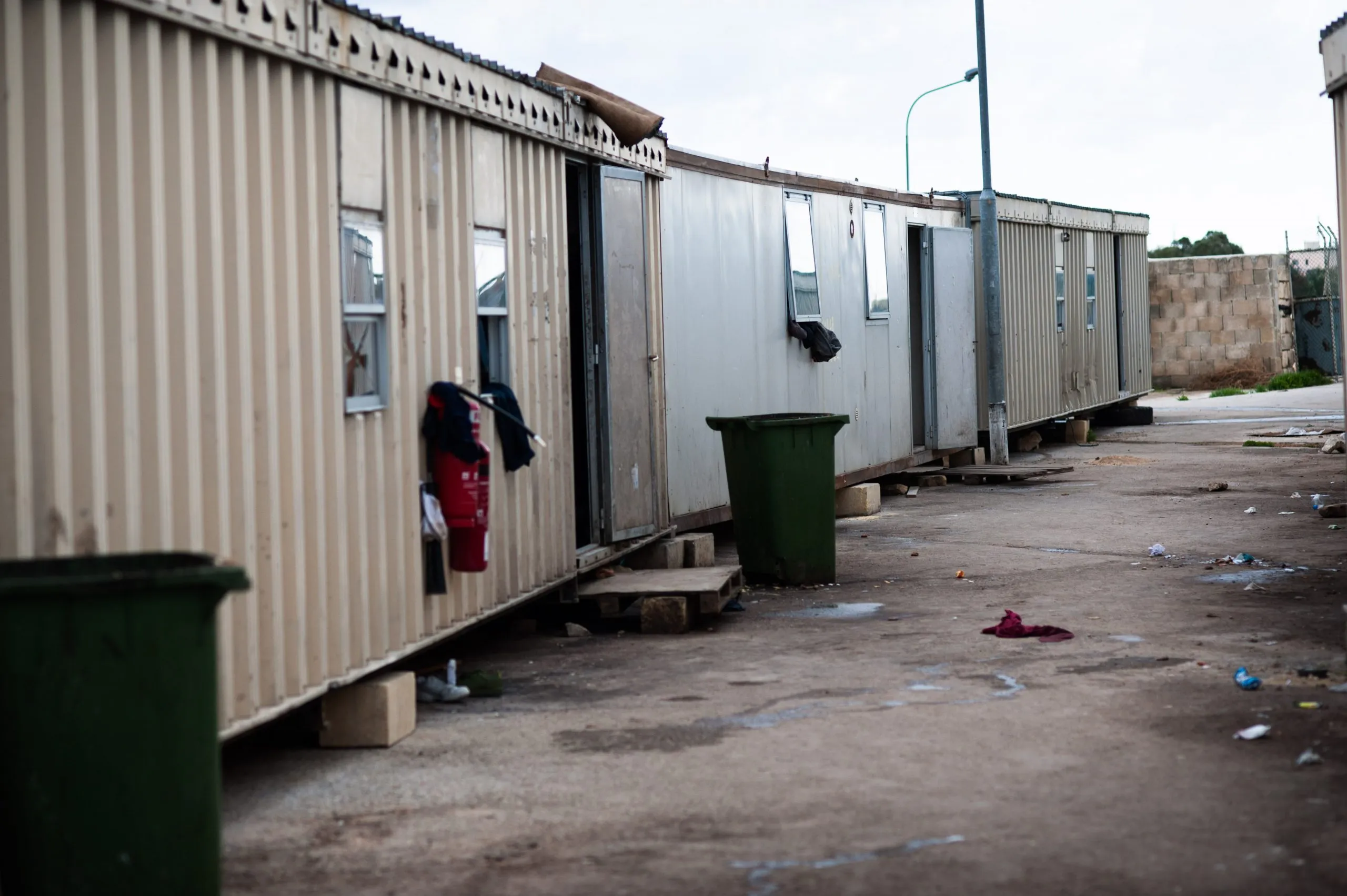 A row of metal container homes with bins and washing outside, at the Malta asylum compound.