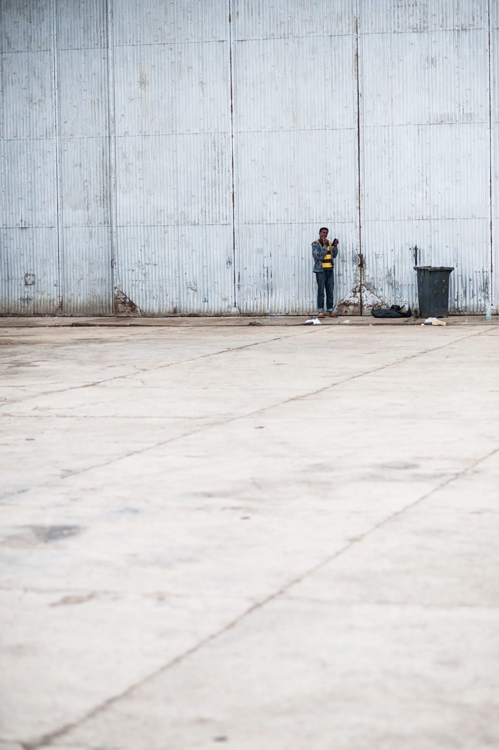A lone figure stands against the vast metal facade of the housing hangar in Malta.