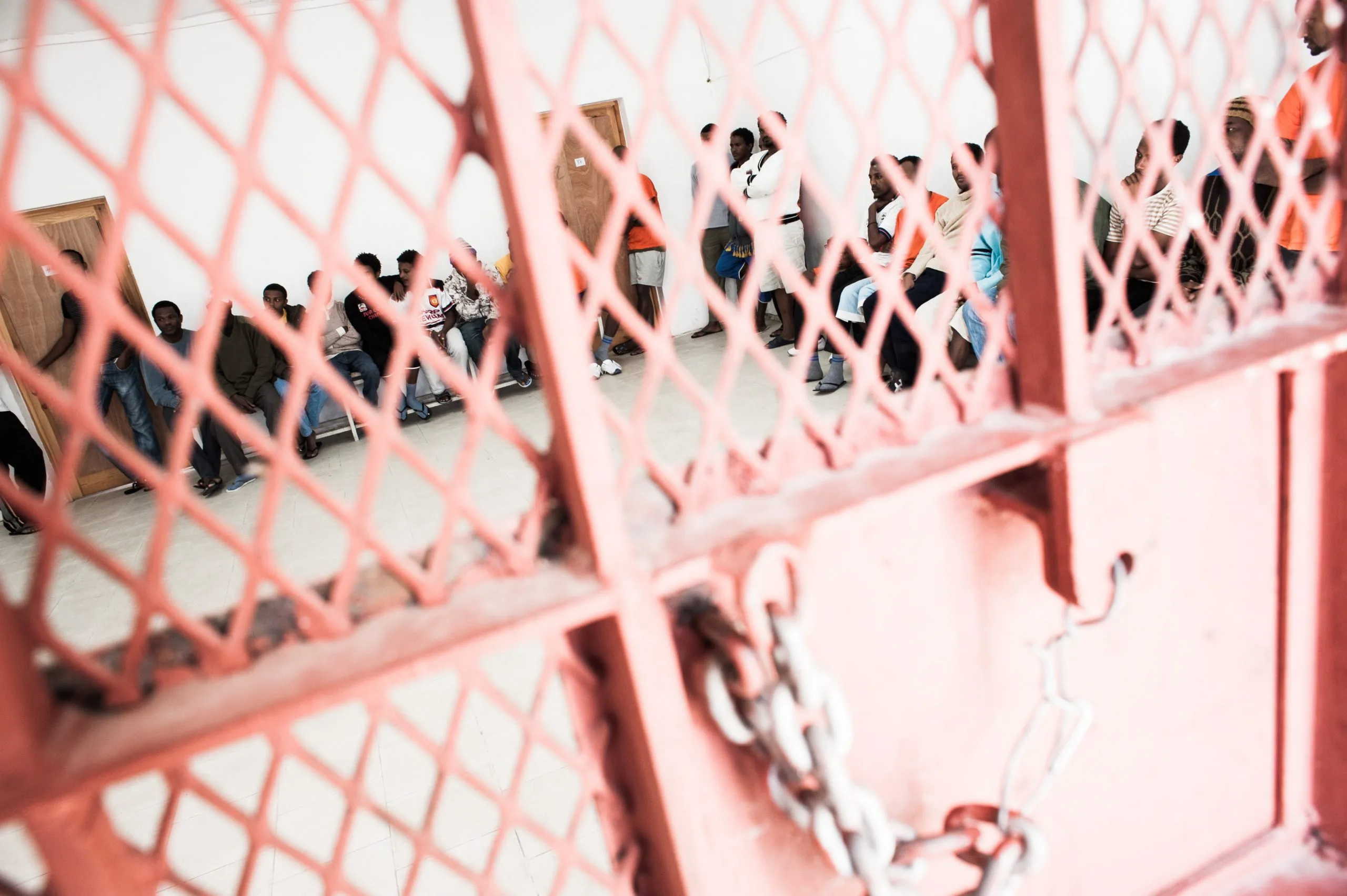 View through a chained pink mesh gate into a holding room at the Malta asylum compound.